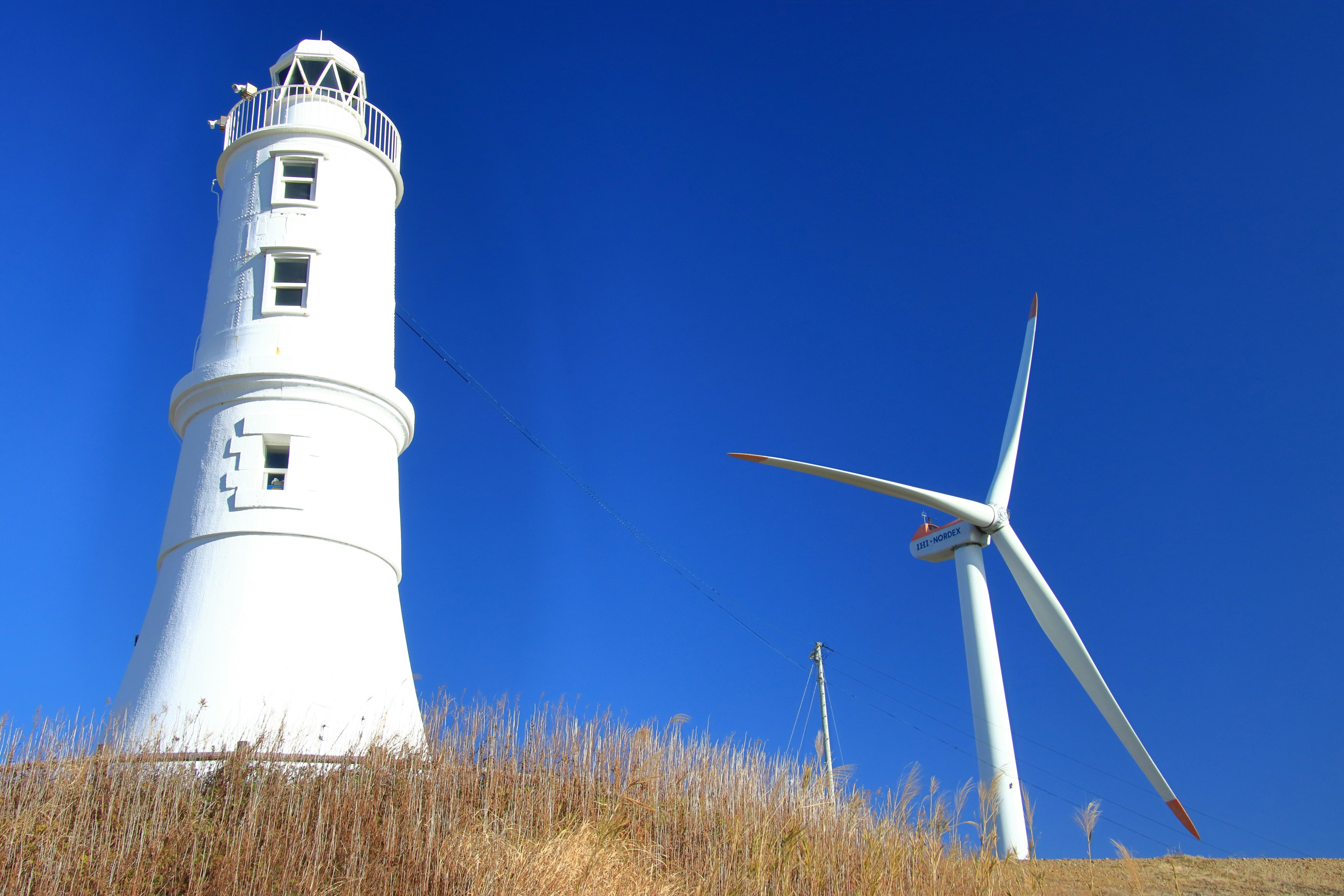 Faro blanco y turbina eólica bajo un cielo azul