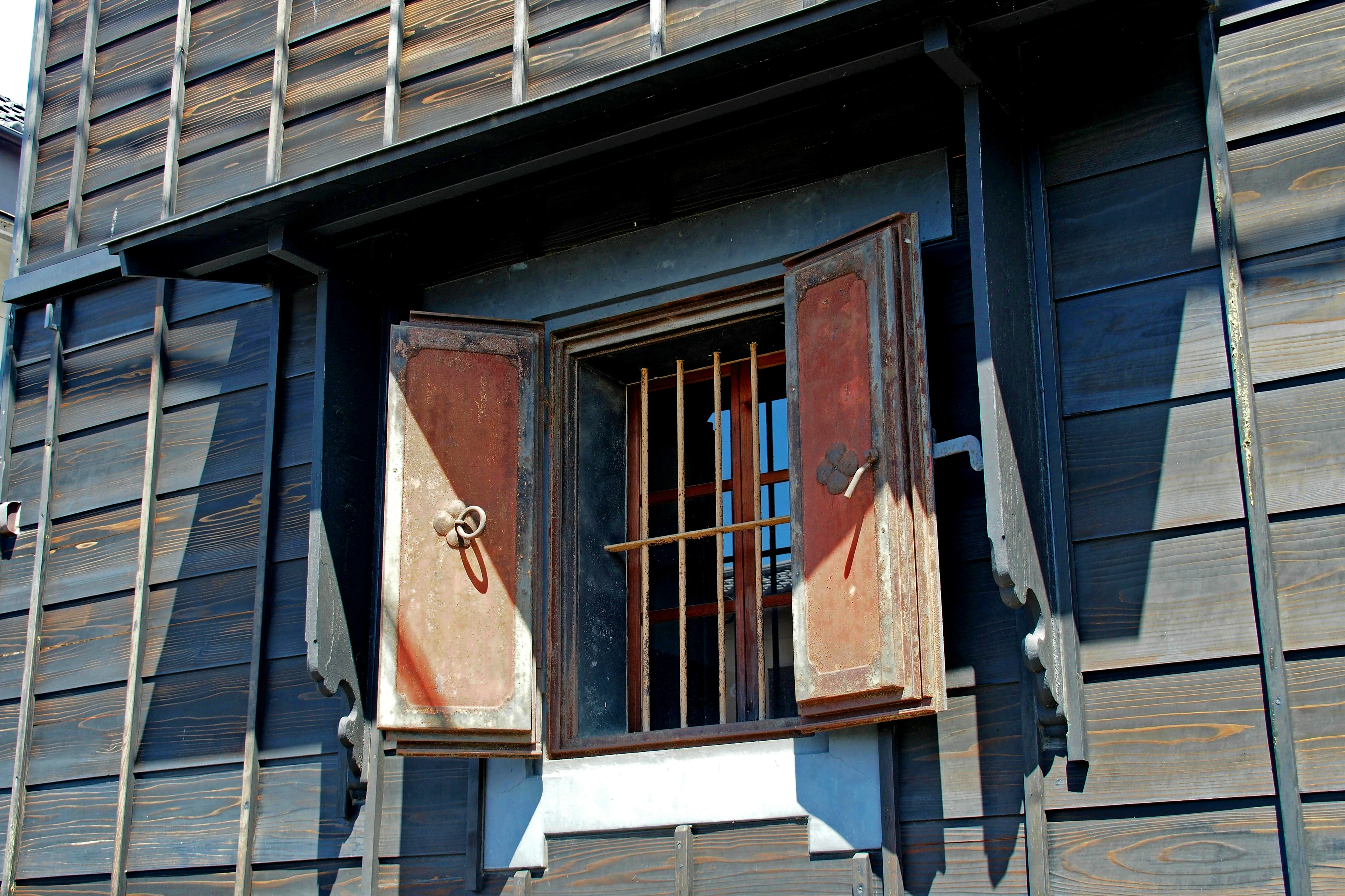 Open window with wooden shutters and bars on an old wooden building