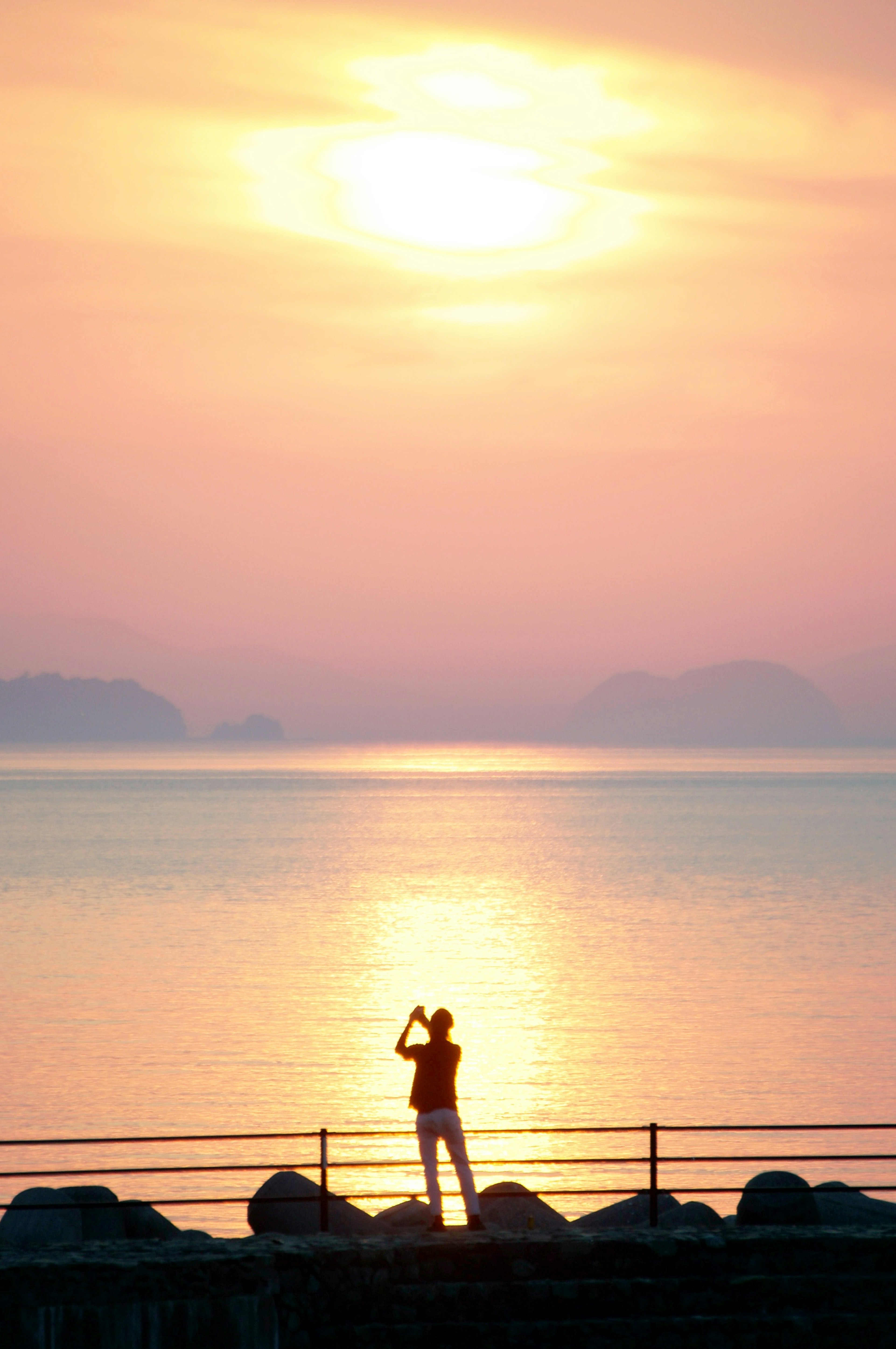 Silhouette seseorang yang menatap laut dengan latar belakang matahari terbenam