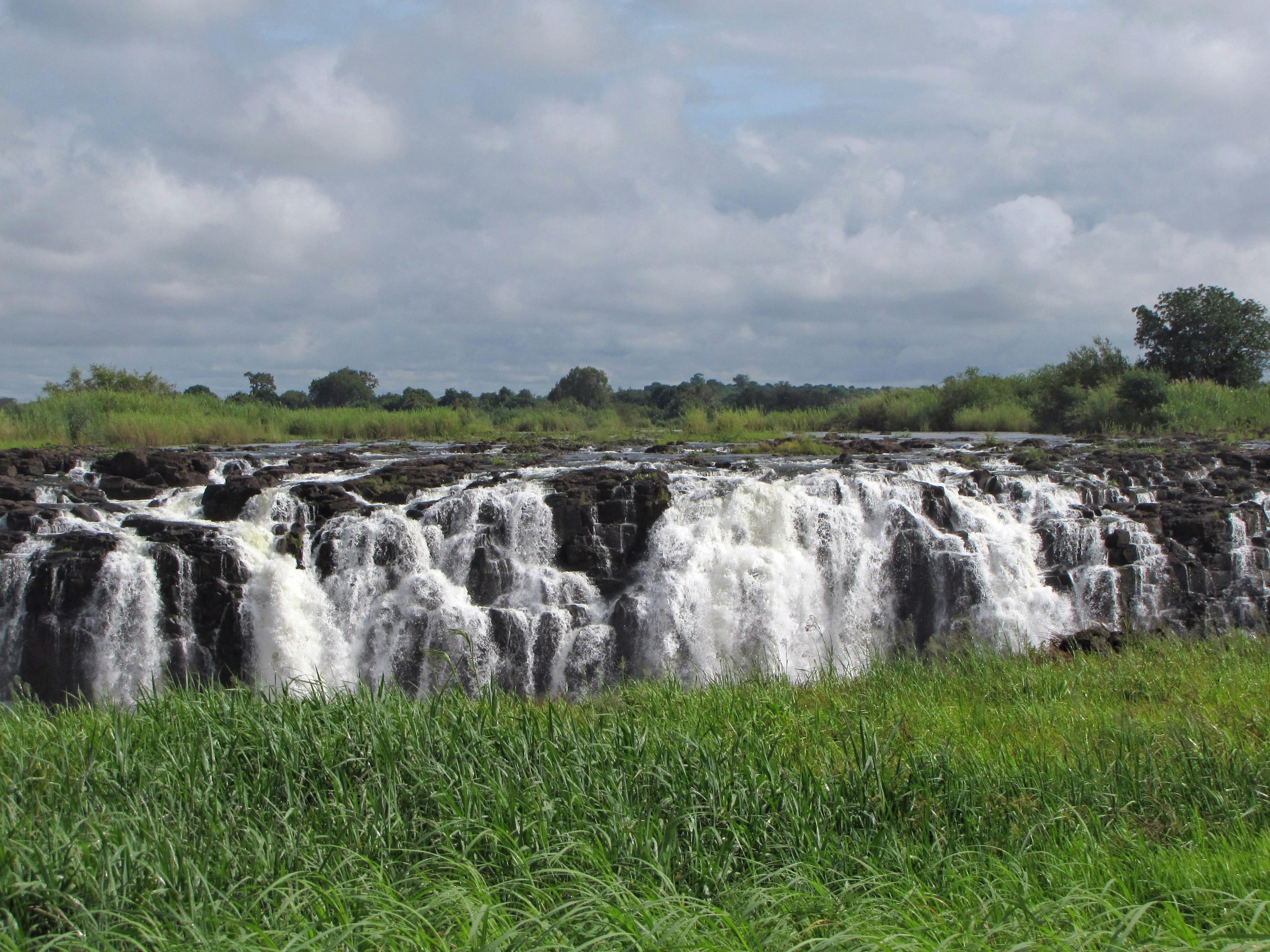 Wasserfall, der über Felsen fließt, umgeben von grünem Gras unter einem bewölkten Himmel