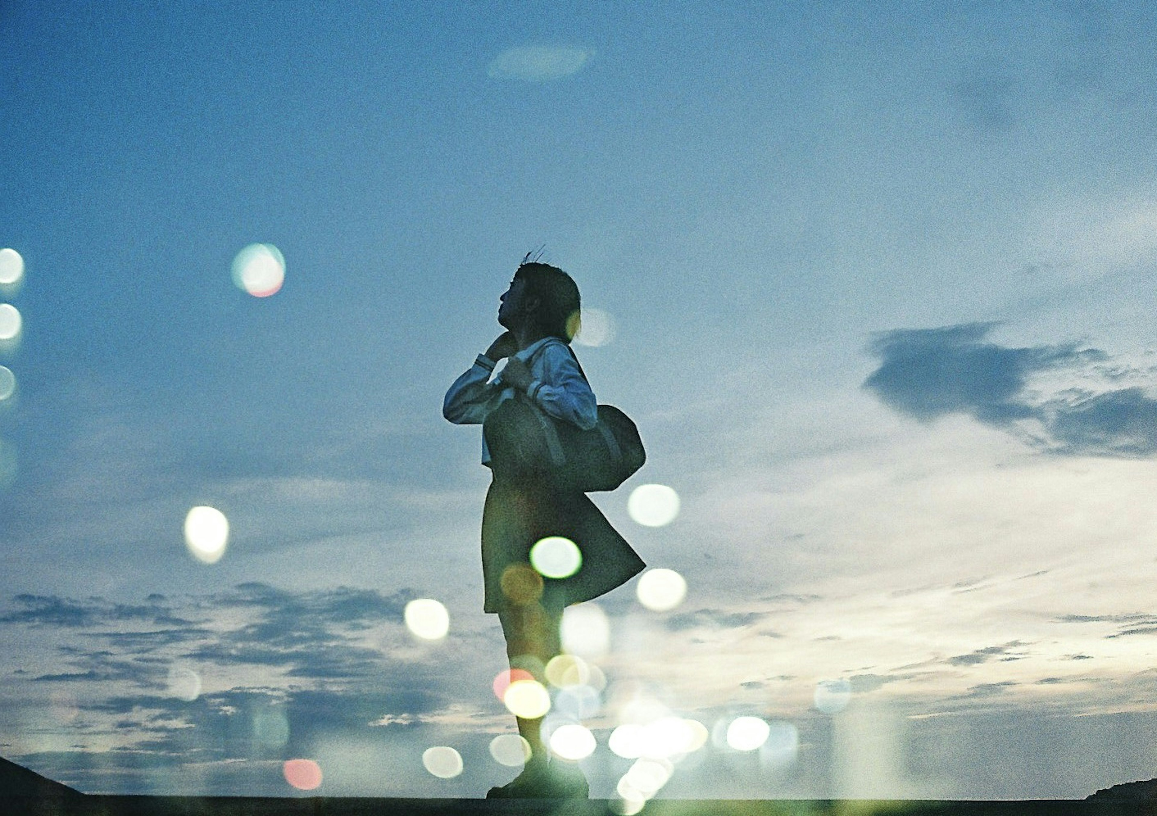 Silhouette seorang wanita berdiri di latar belakang langit senja dengan cahaya kabur