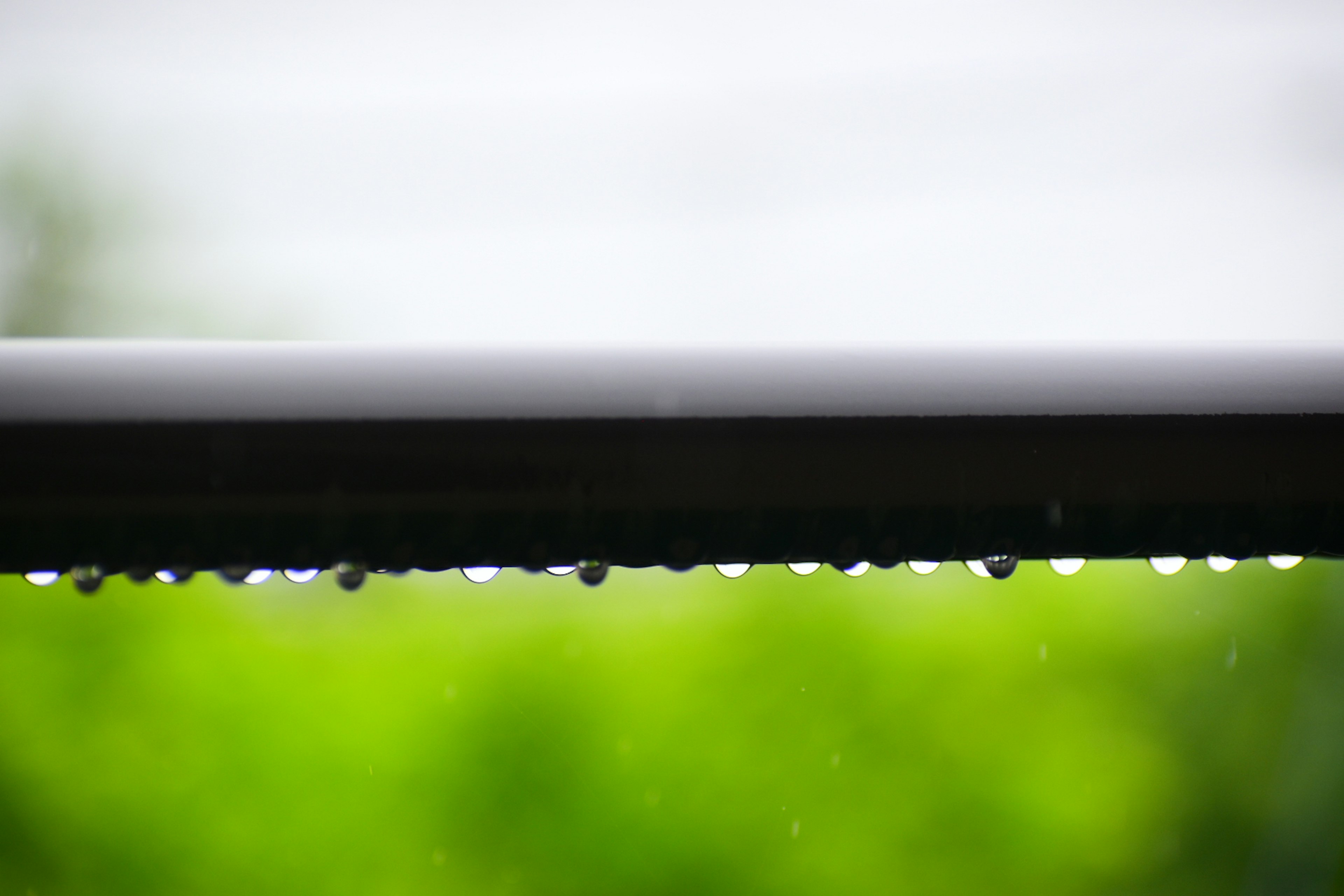 Raindrops on a roof edge with a blurred green background