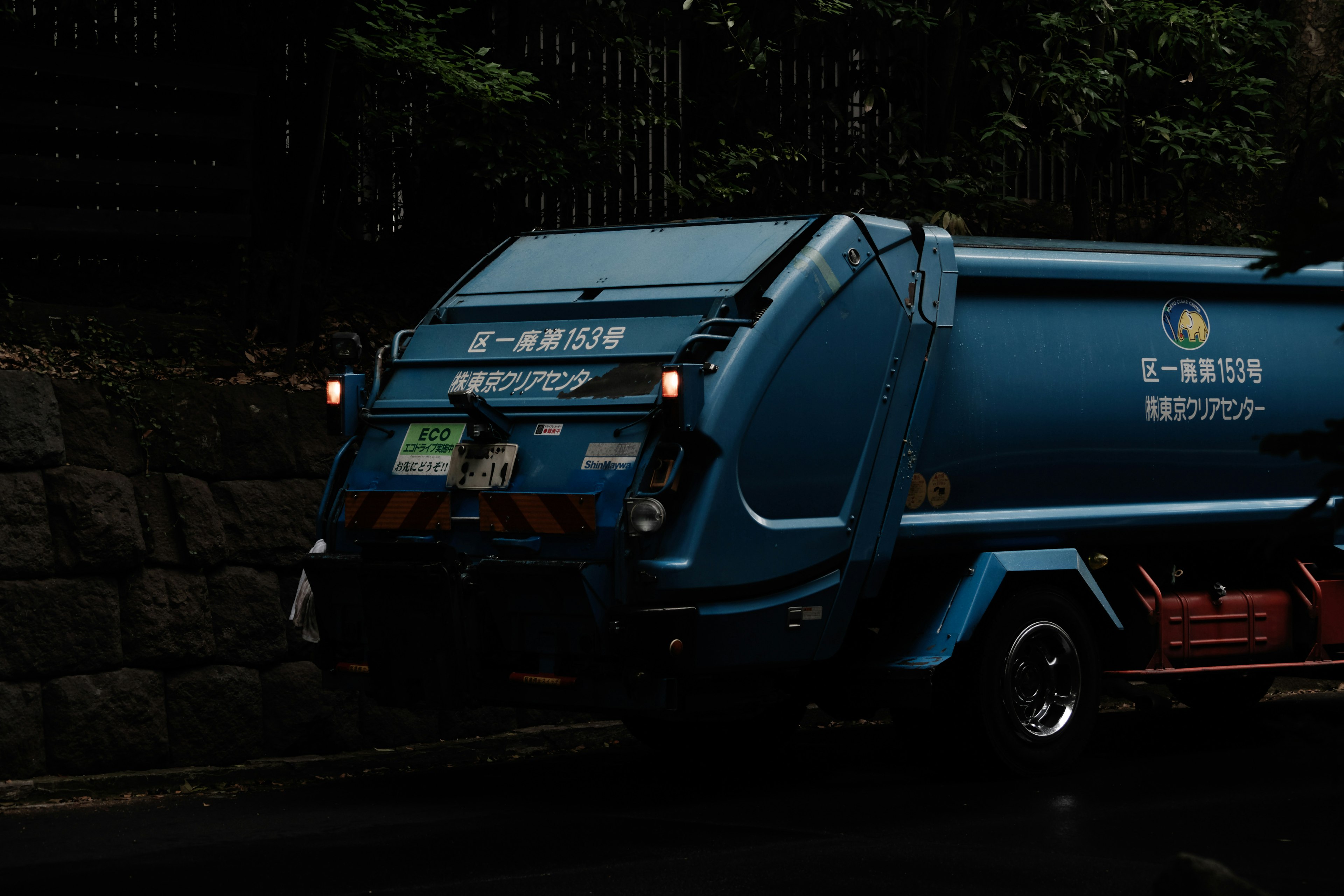 Un camion poubelle bleu garé devant un mur en pierre