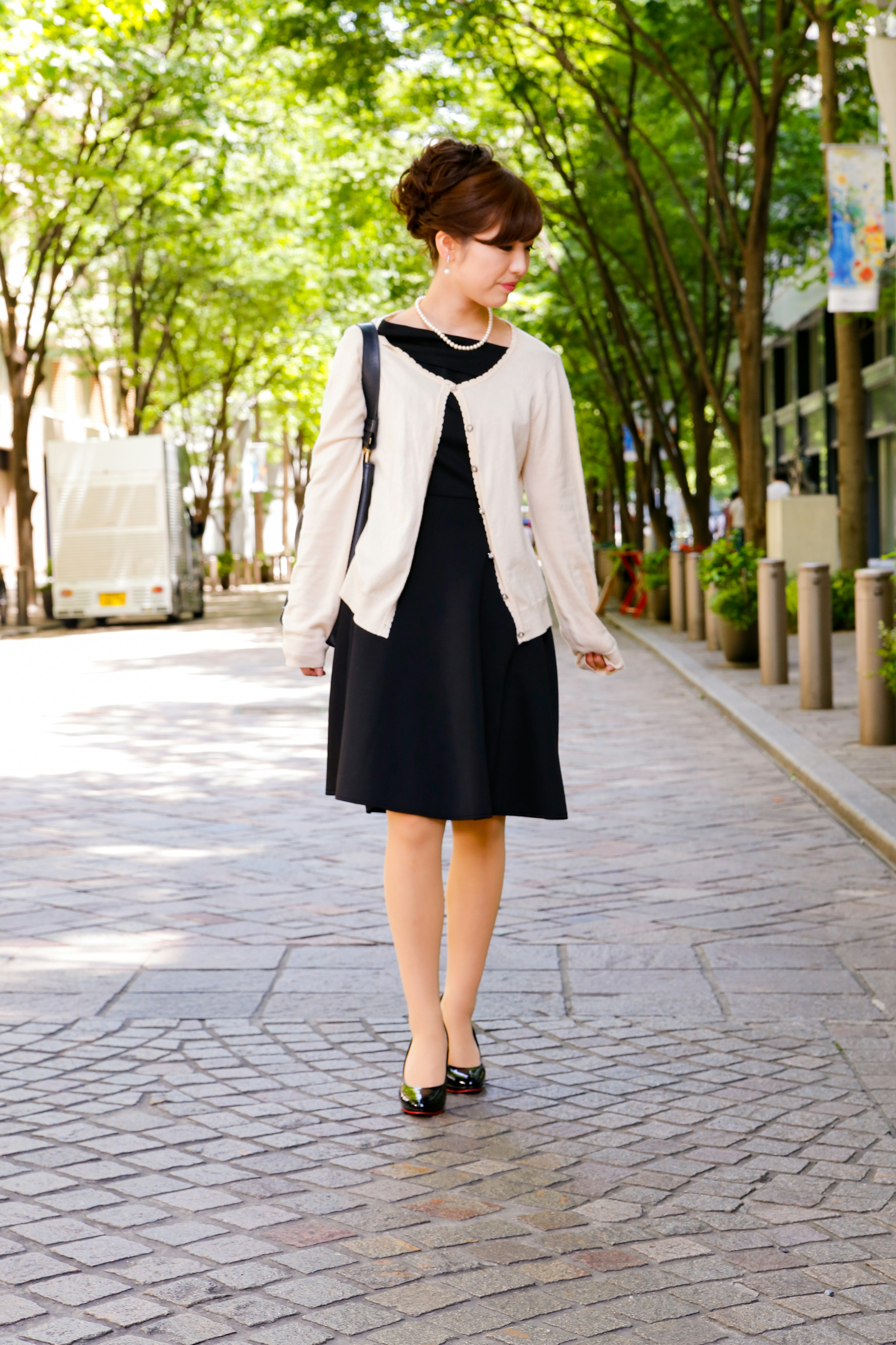 Une femme portant une robe noire et un cardigan beige marchant dans la rue