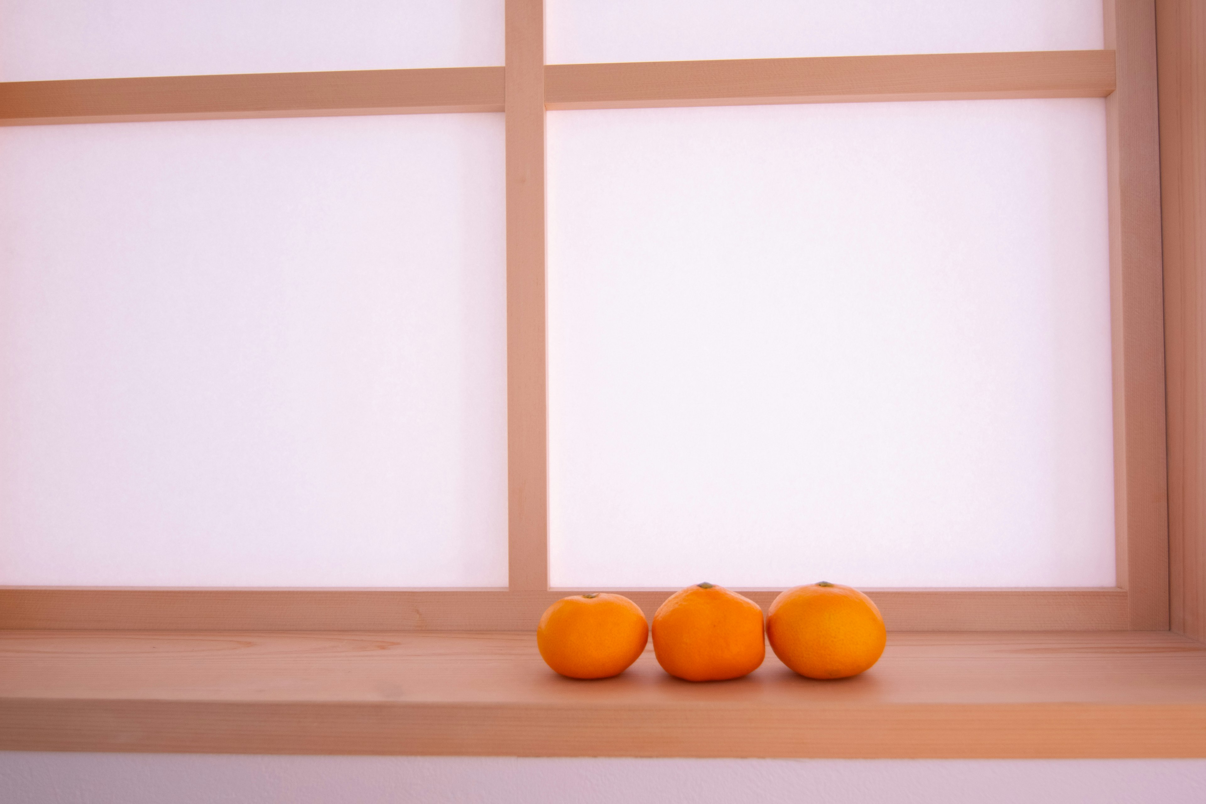 Trois oranges posées sur un rebord de fenêtre en bois avec un fond doux