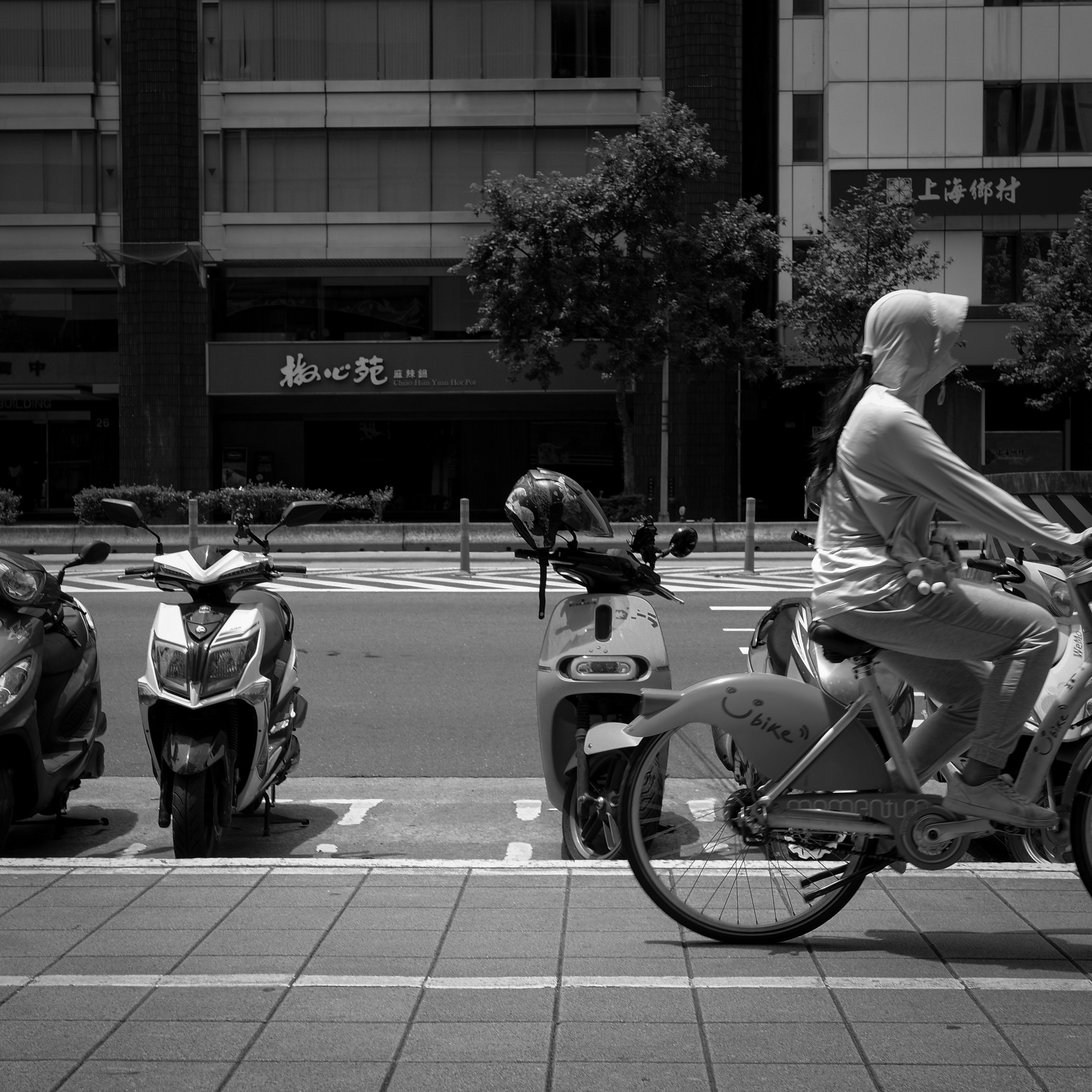 A woman riding a bicycle alongside parked scooters in an urban setting
