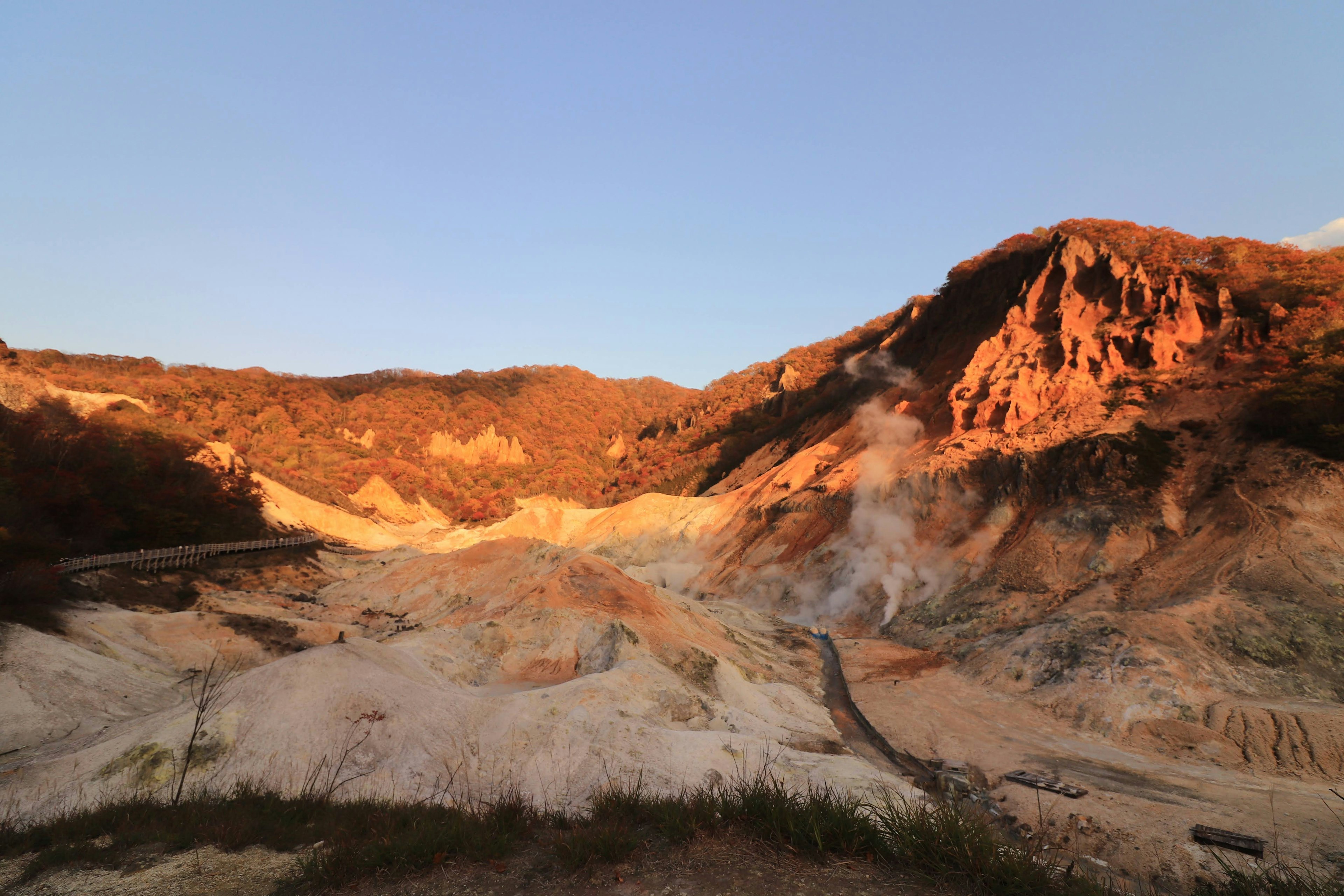 Panoramablick auf ein geothermisches Gebiet bei Sonnenuntergang Dampf steigt von heißen Quellen auf Lebendiger orange-blauer Himmel