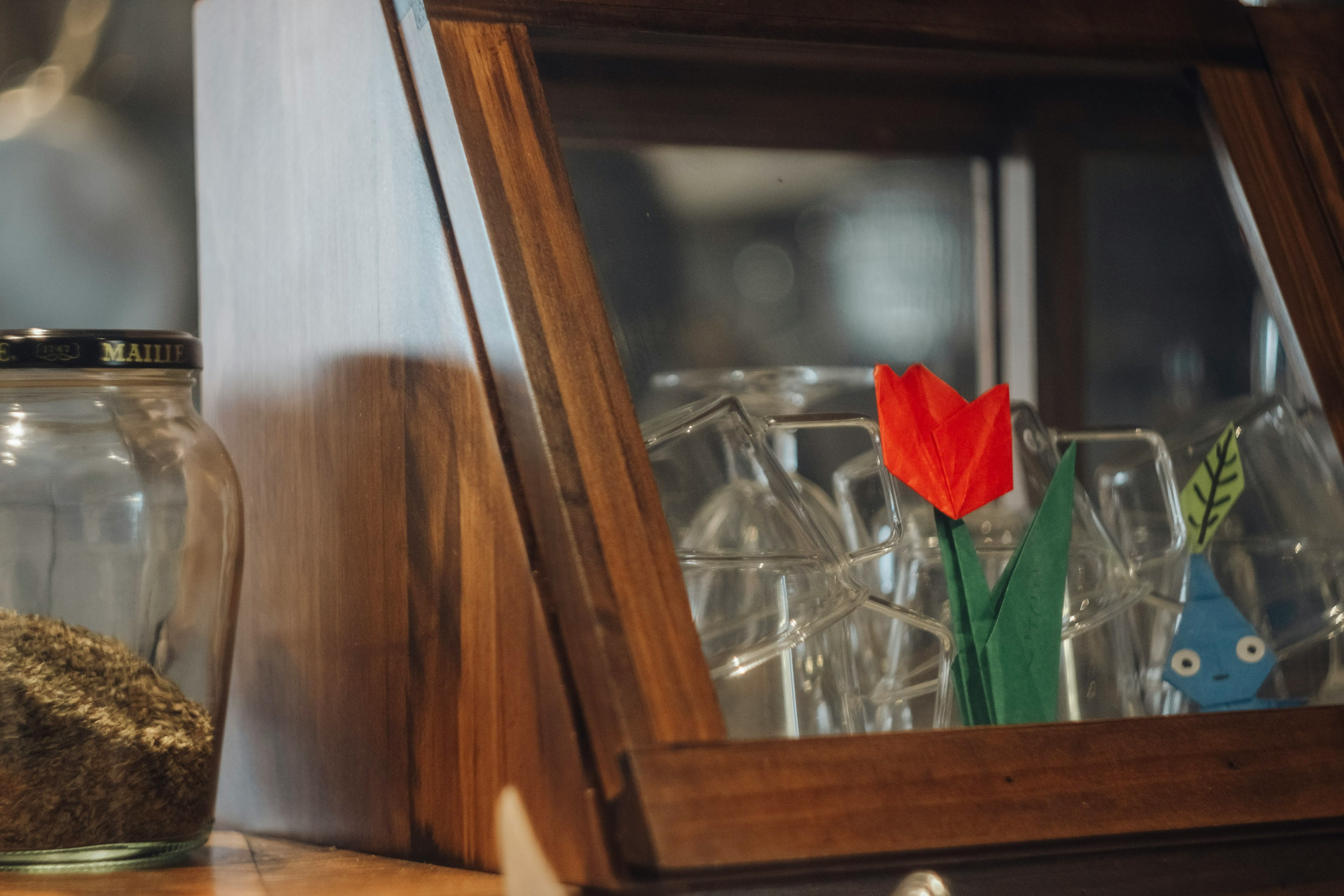 Un armario de madera que muestra cristalería y una flor de tulipán rojo