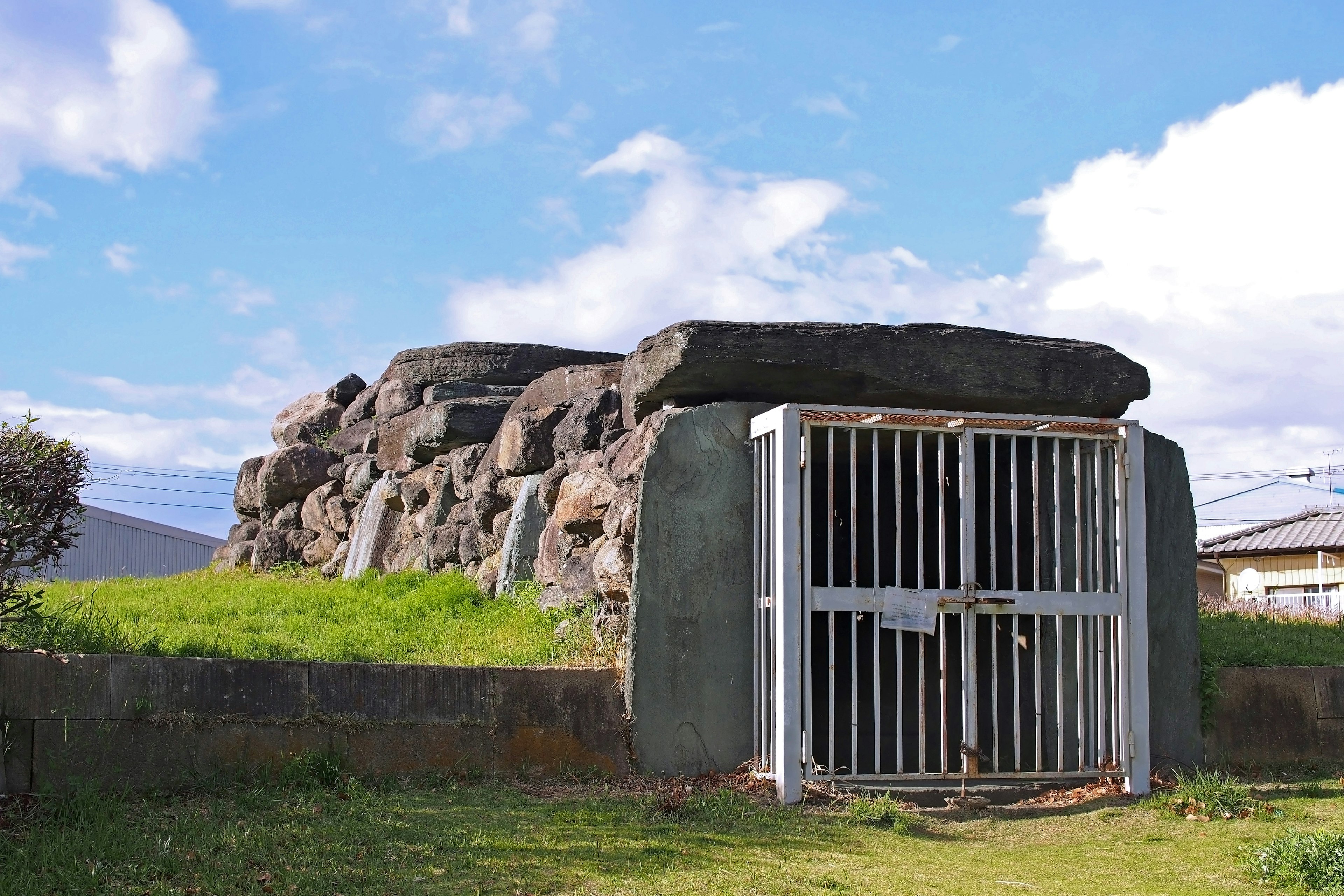 Túmulo antiguo de piedra con una puerta de metal en un paisaje de hierba verde