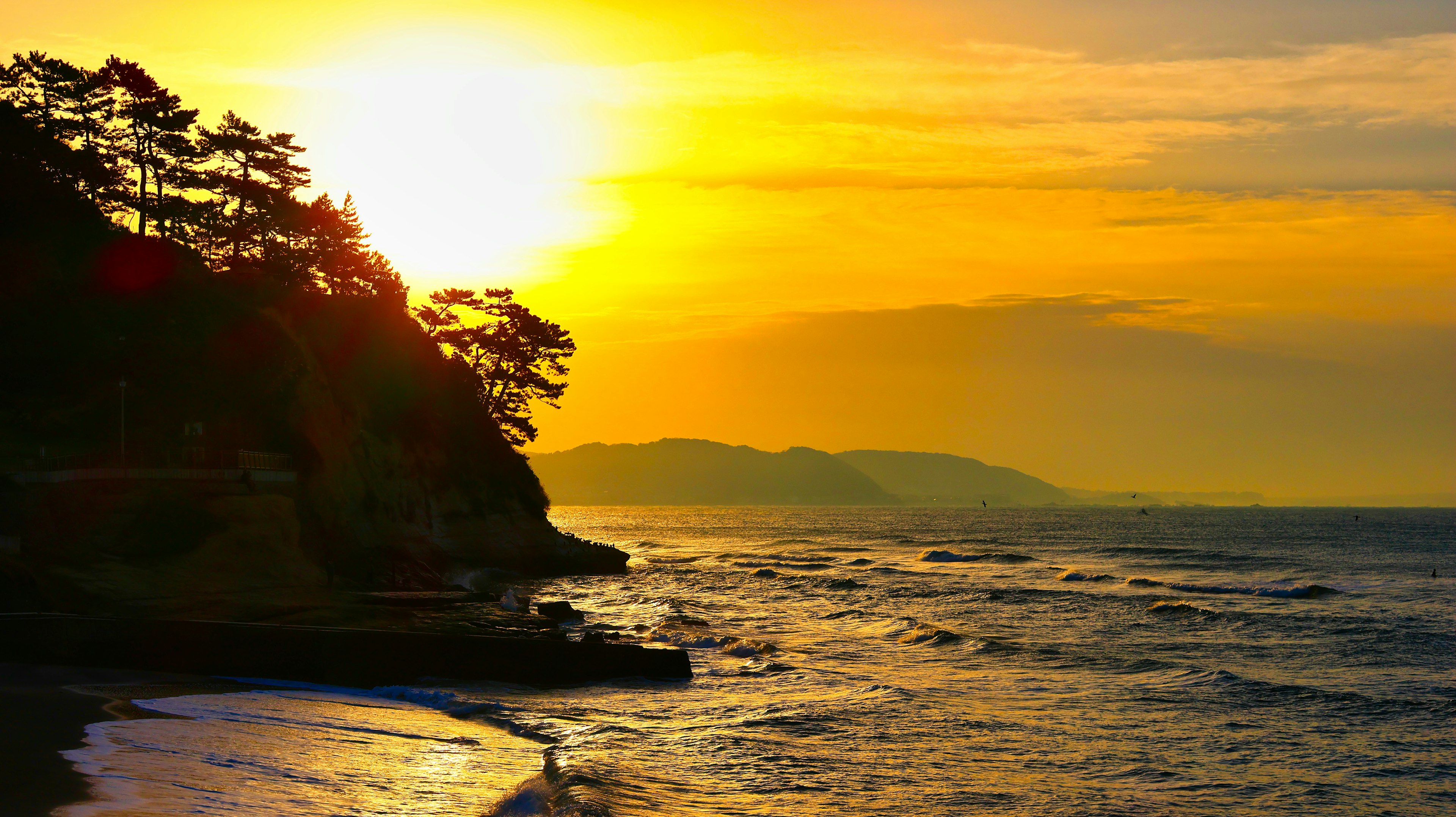 Pemandangan indah matahari terbenam di atas lautan dengan pepohonan hijau di sepanjang pantai