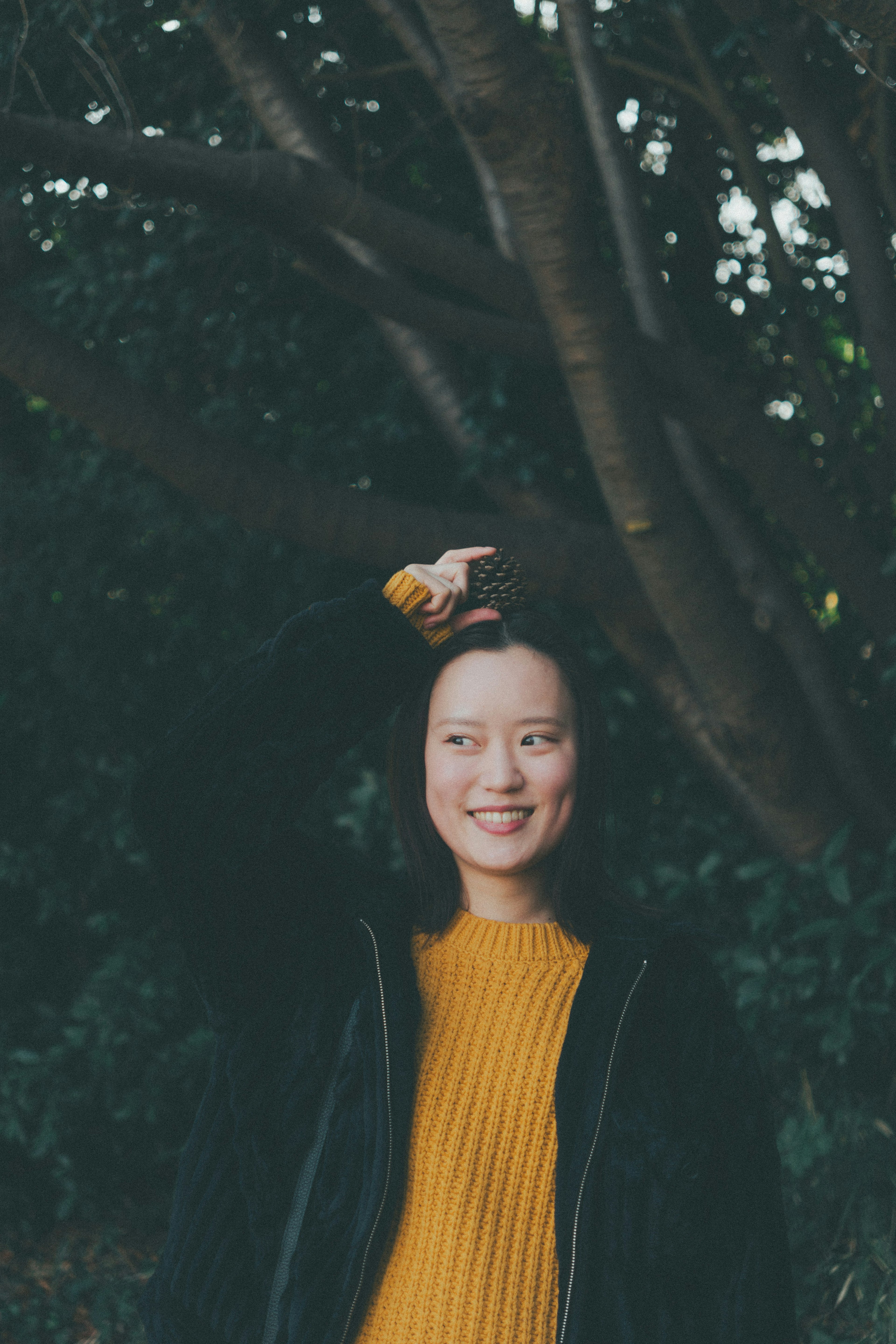 Donna sorridente in un maglione giallo brillante davanti a uno sfondo di alberi