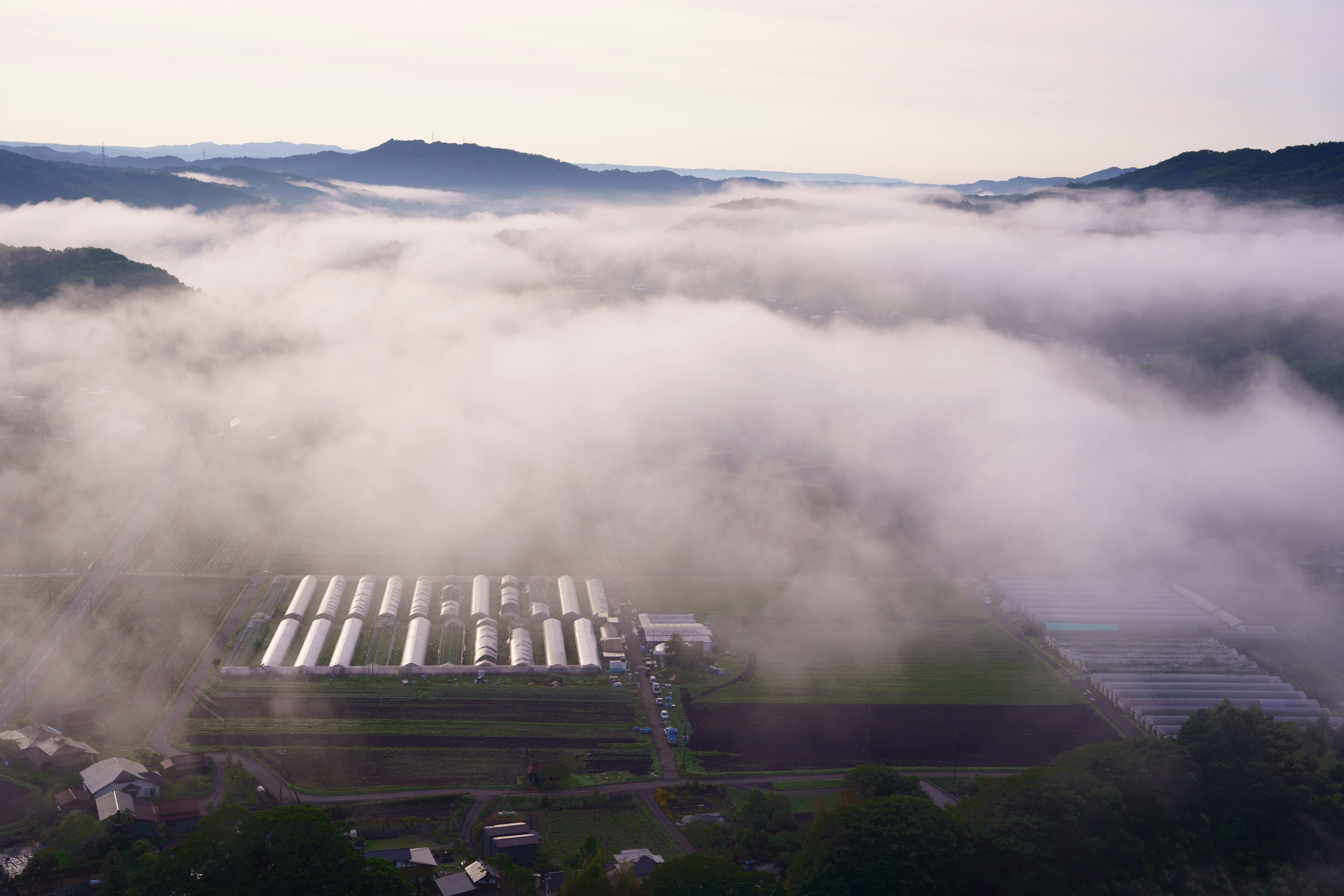 Aerial view of a farm shrouded in fog surrounded by faint hills