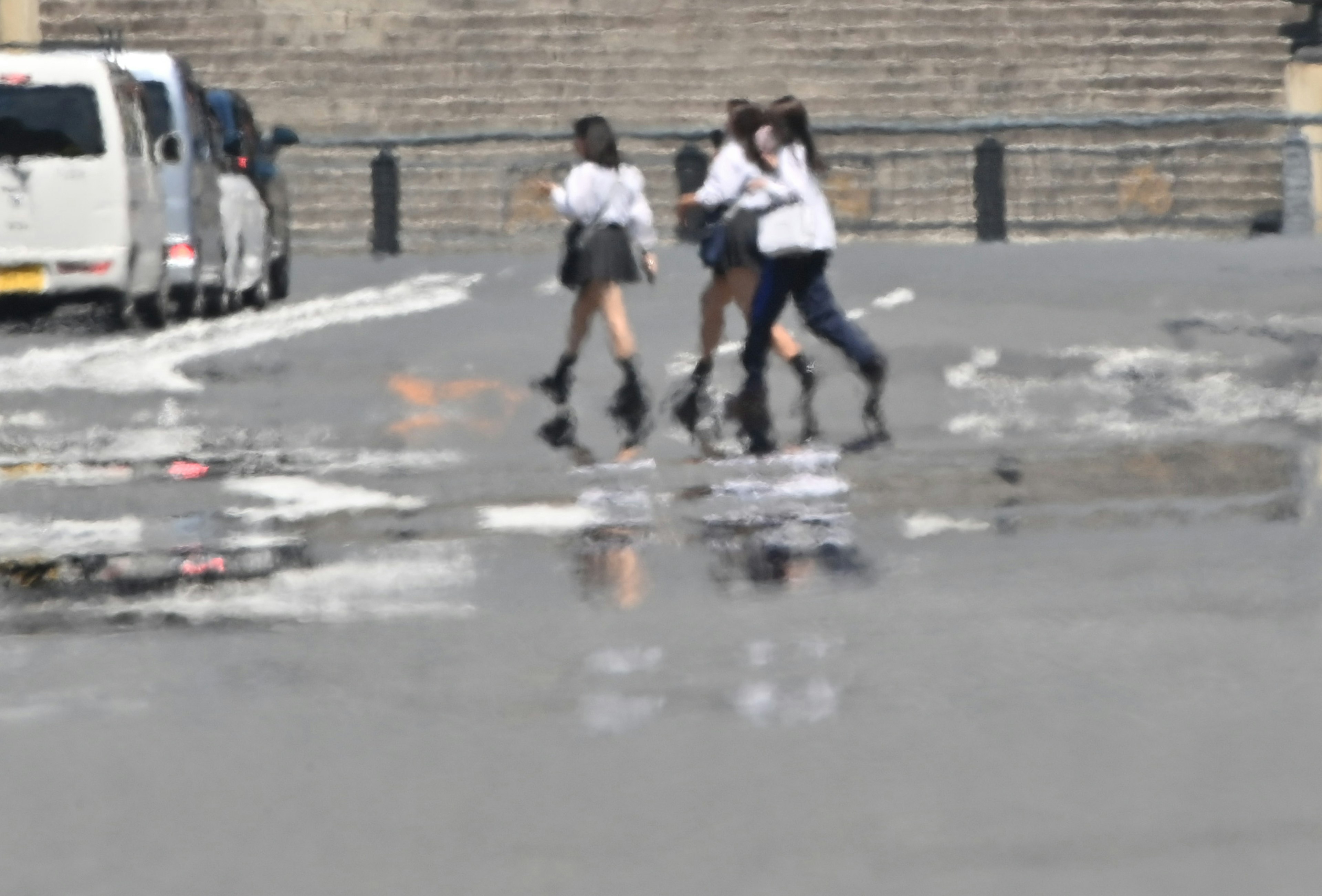 雨上がりの街で白いシャツとスカートを着た女子学生たちが歩いている