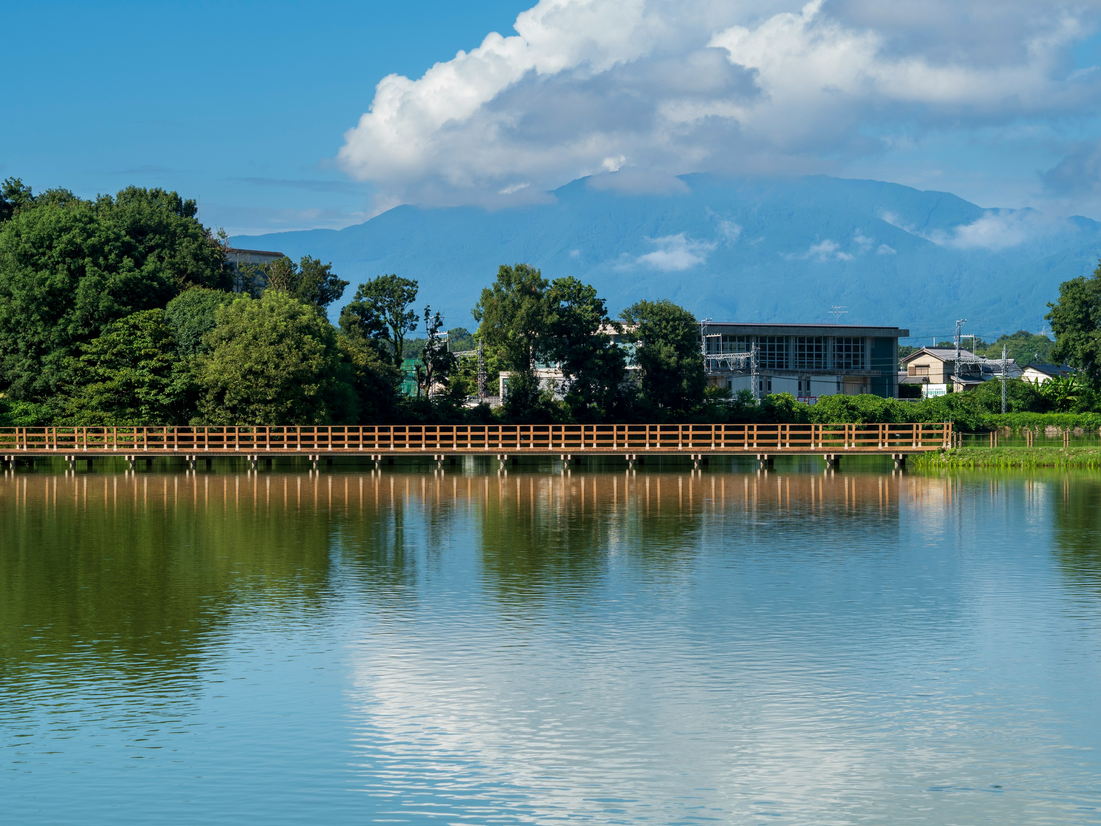 Danau tenang yang mencerminkan langit biru dan awan putih dengan pegunungan di latar belakang