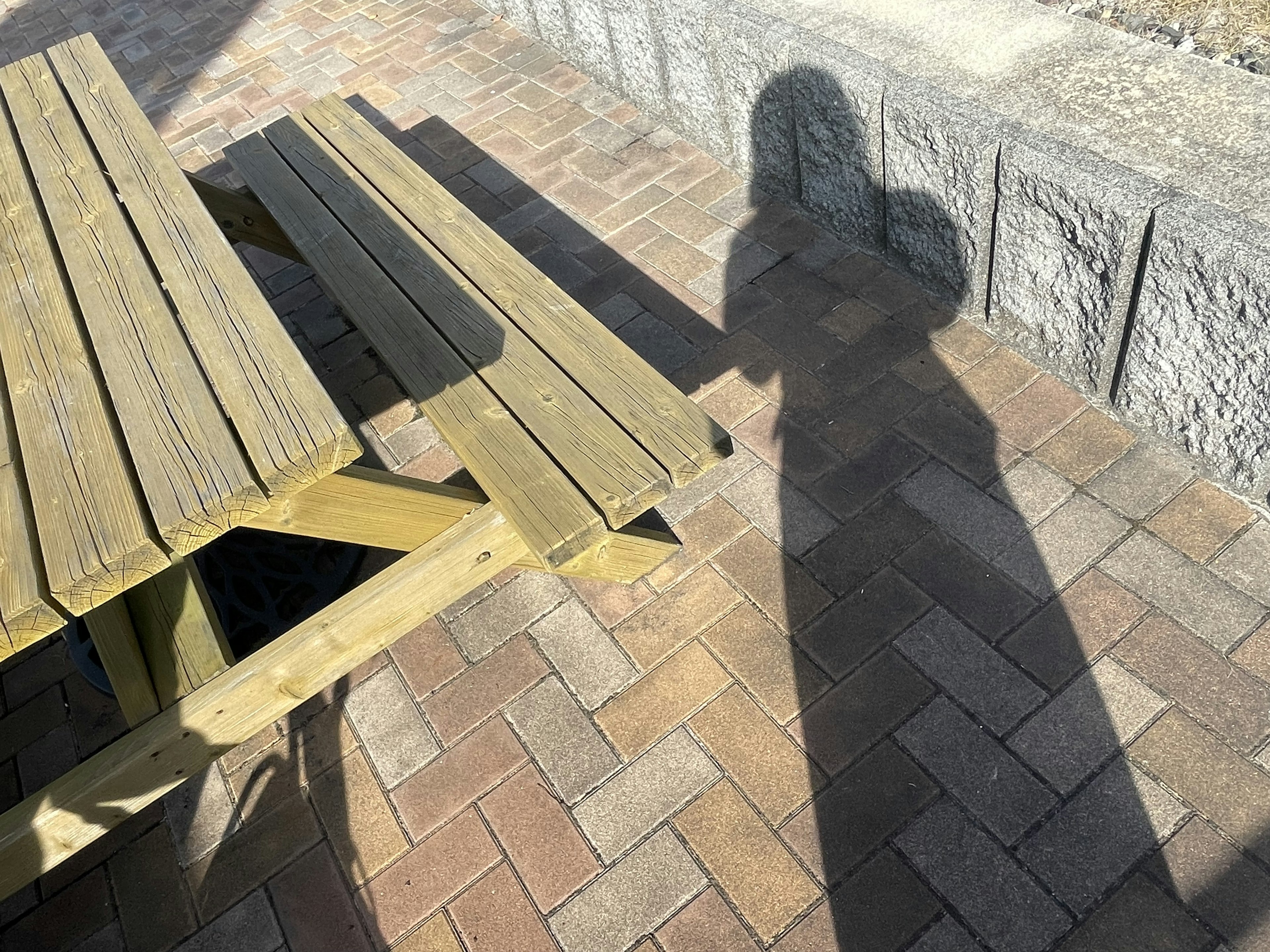 Ombre projetée sur un sol en briques à côté d'une table de pique-nique en bois