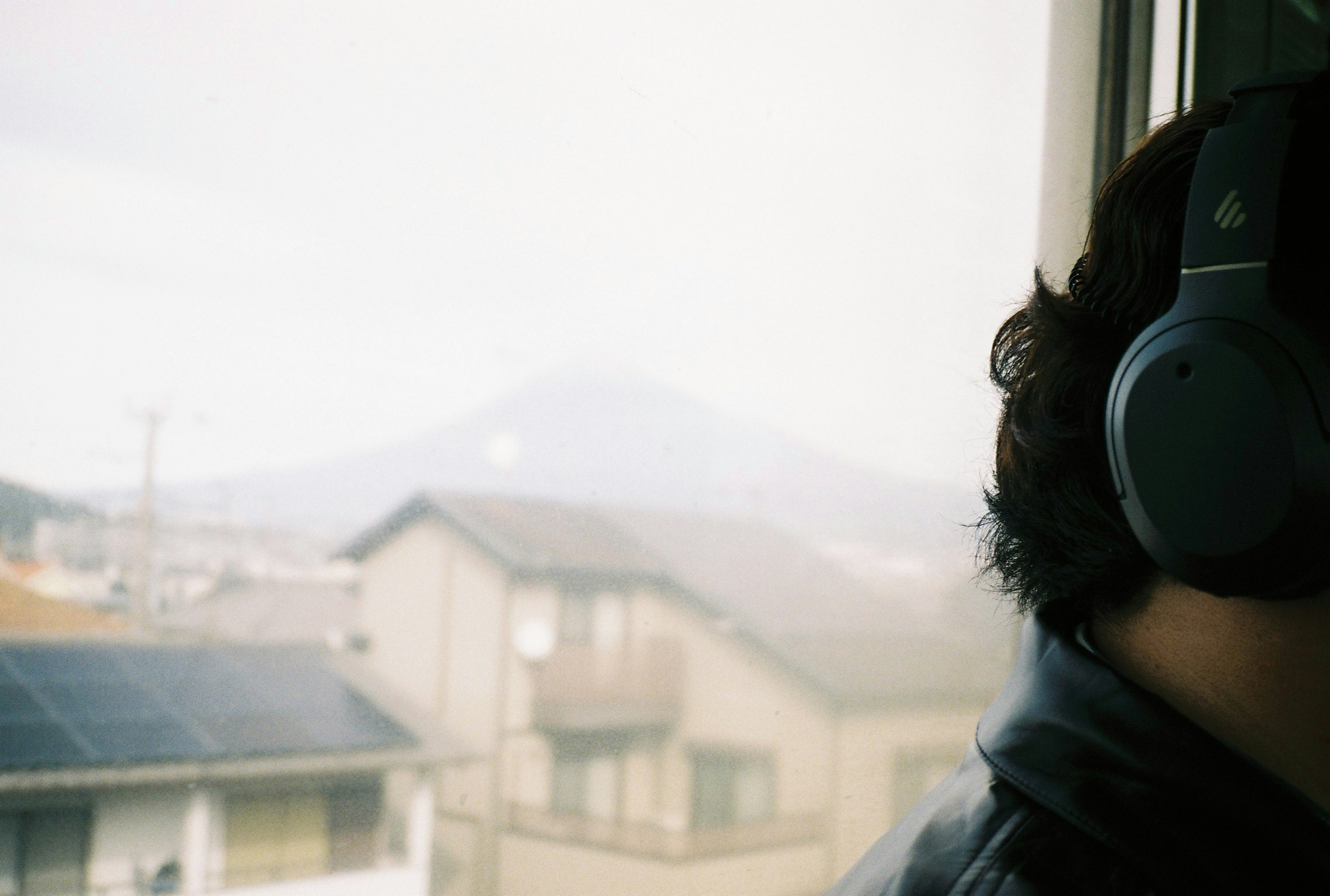 A person wearing headphones with Mount Fuji visible in the background through a window