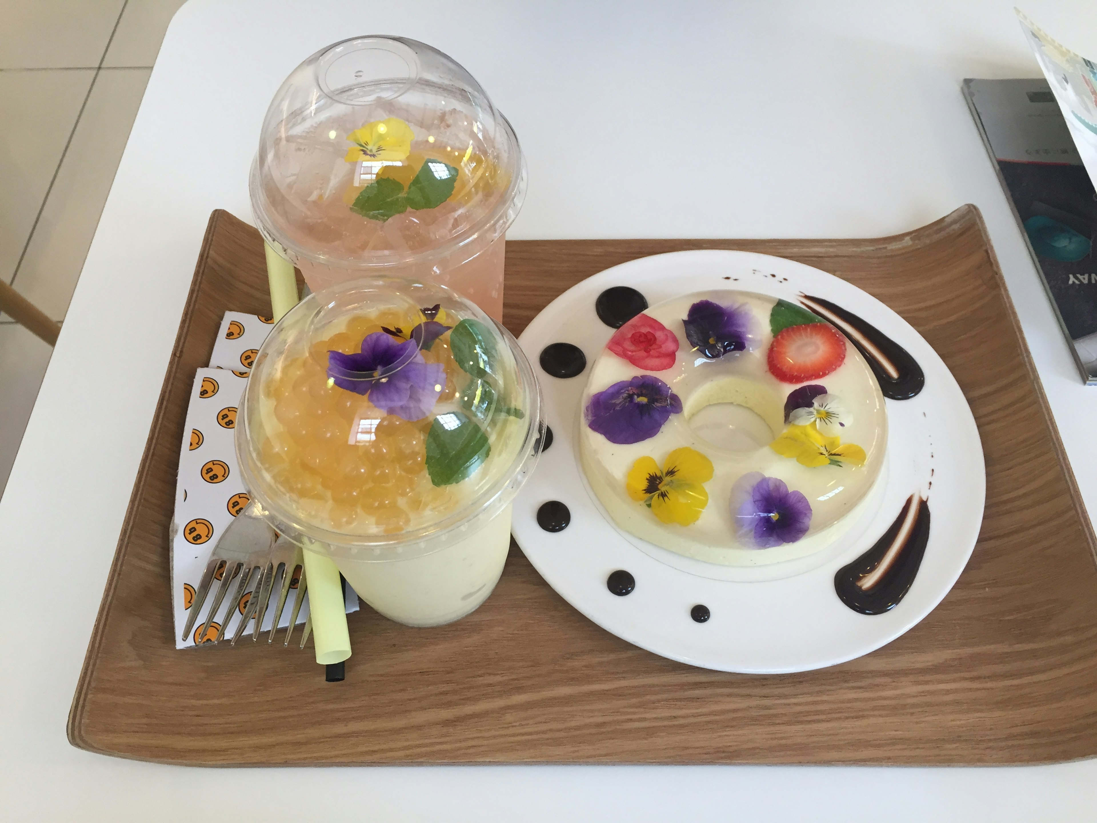 Colorful drinks and a floral dessert arranged on a wooden tray