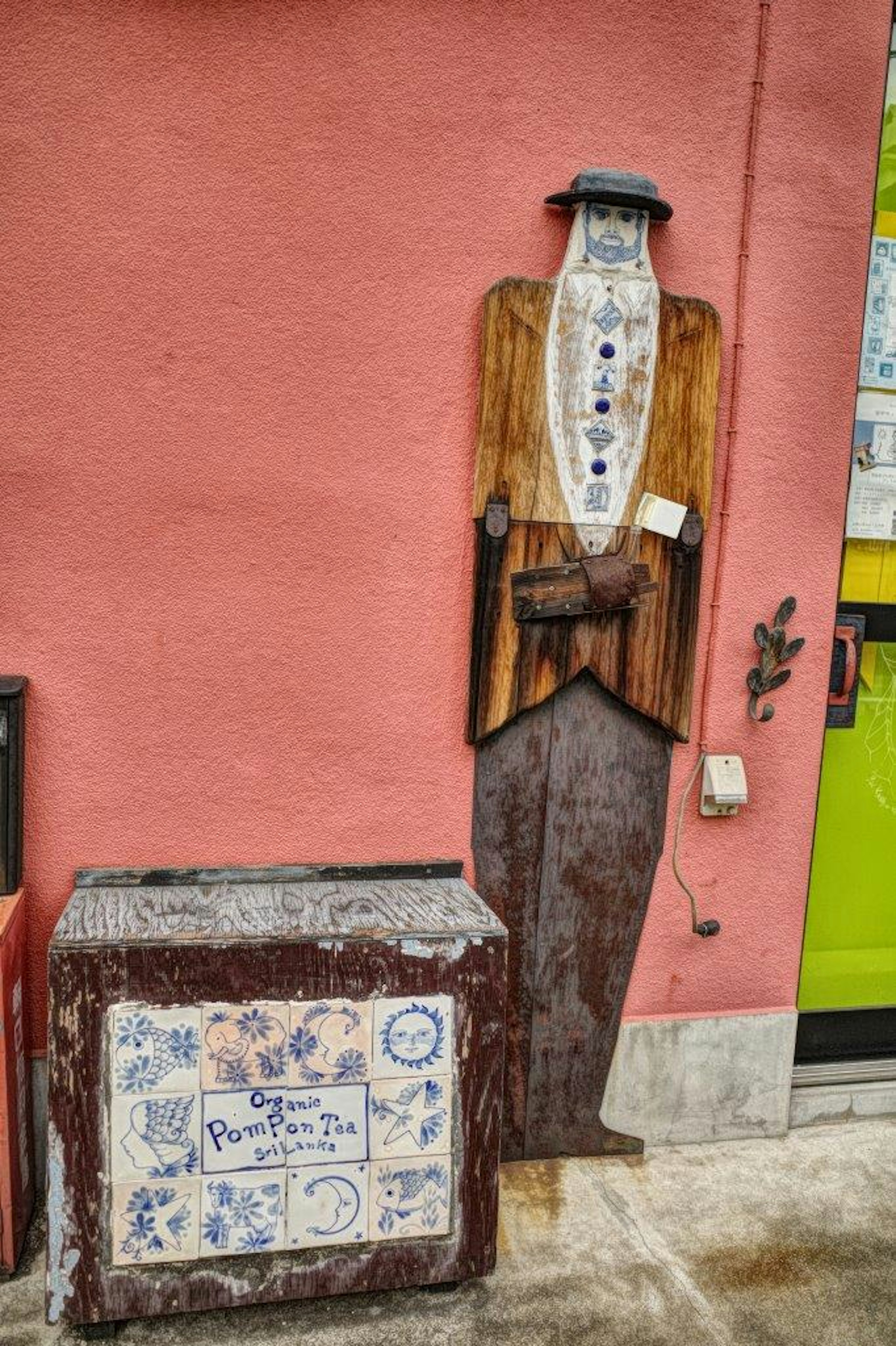 Figure en bois habillée en costume contre un mur rose avec une boîte décorative