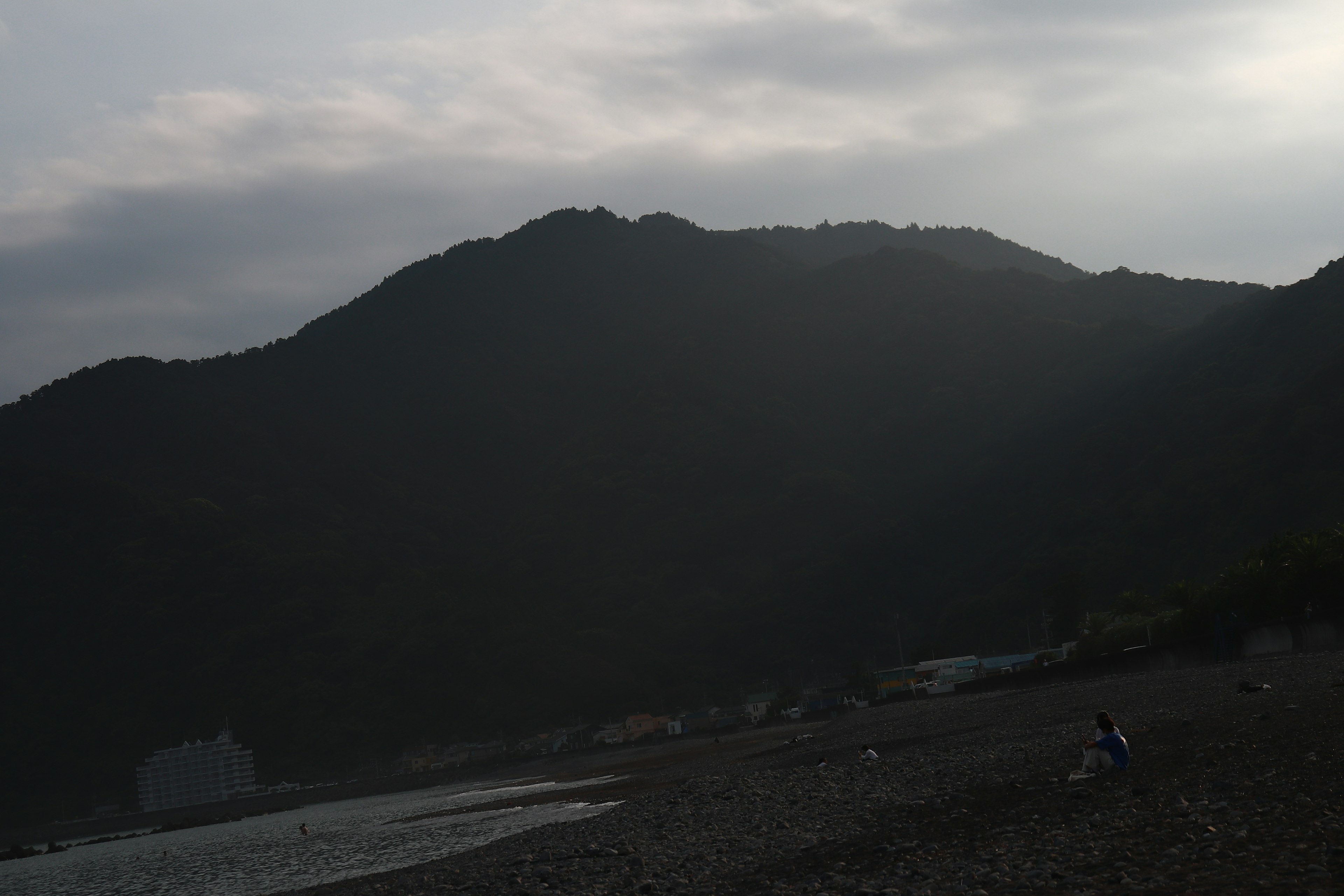 Pemandangan pantai dengan gunung dan langit mendung