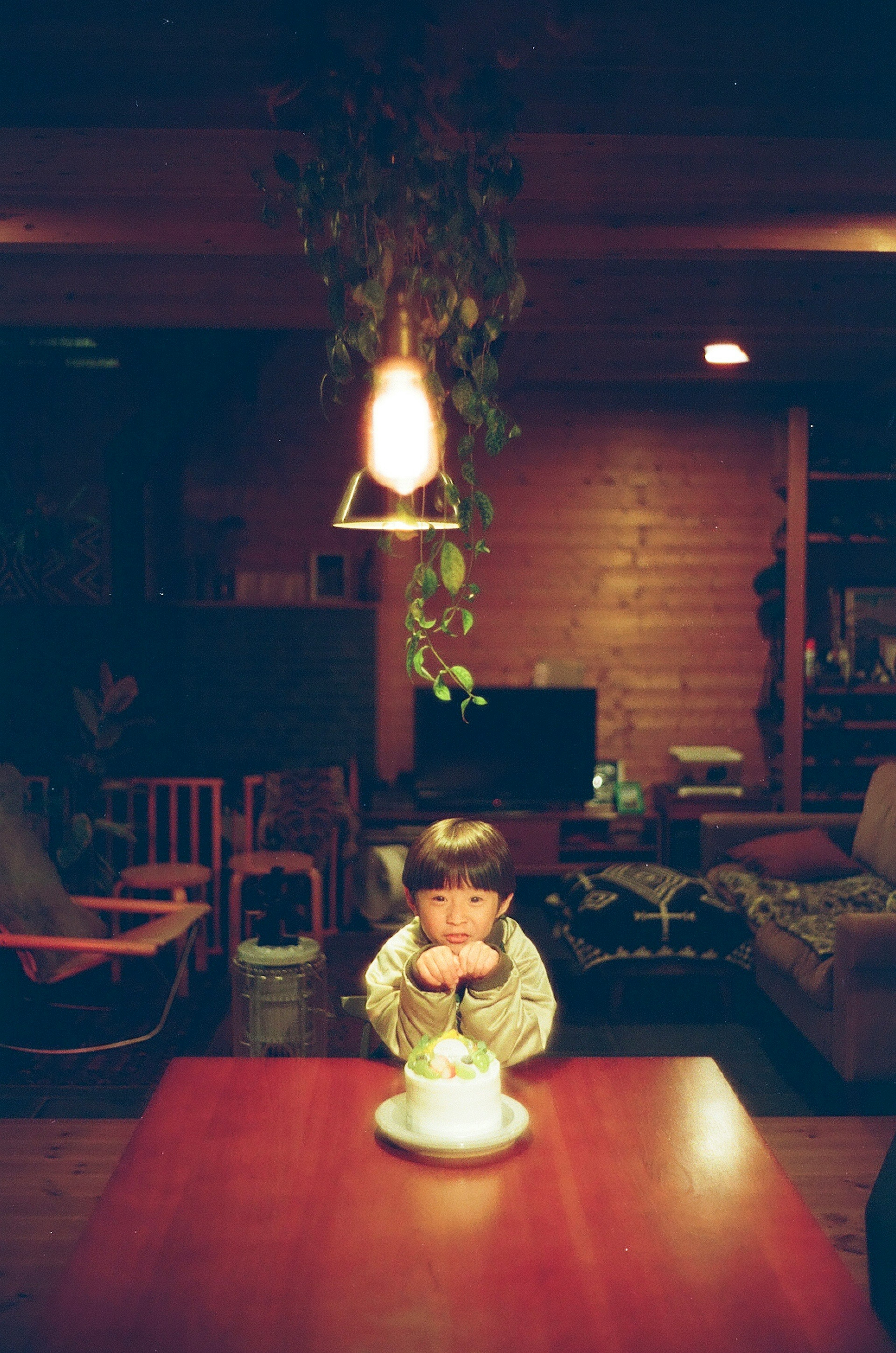 Child sitting at a table with a cake in a dimly lit room