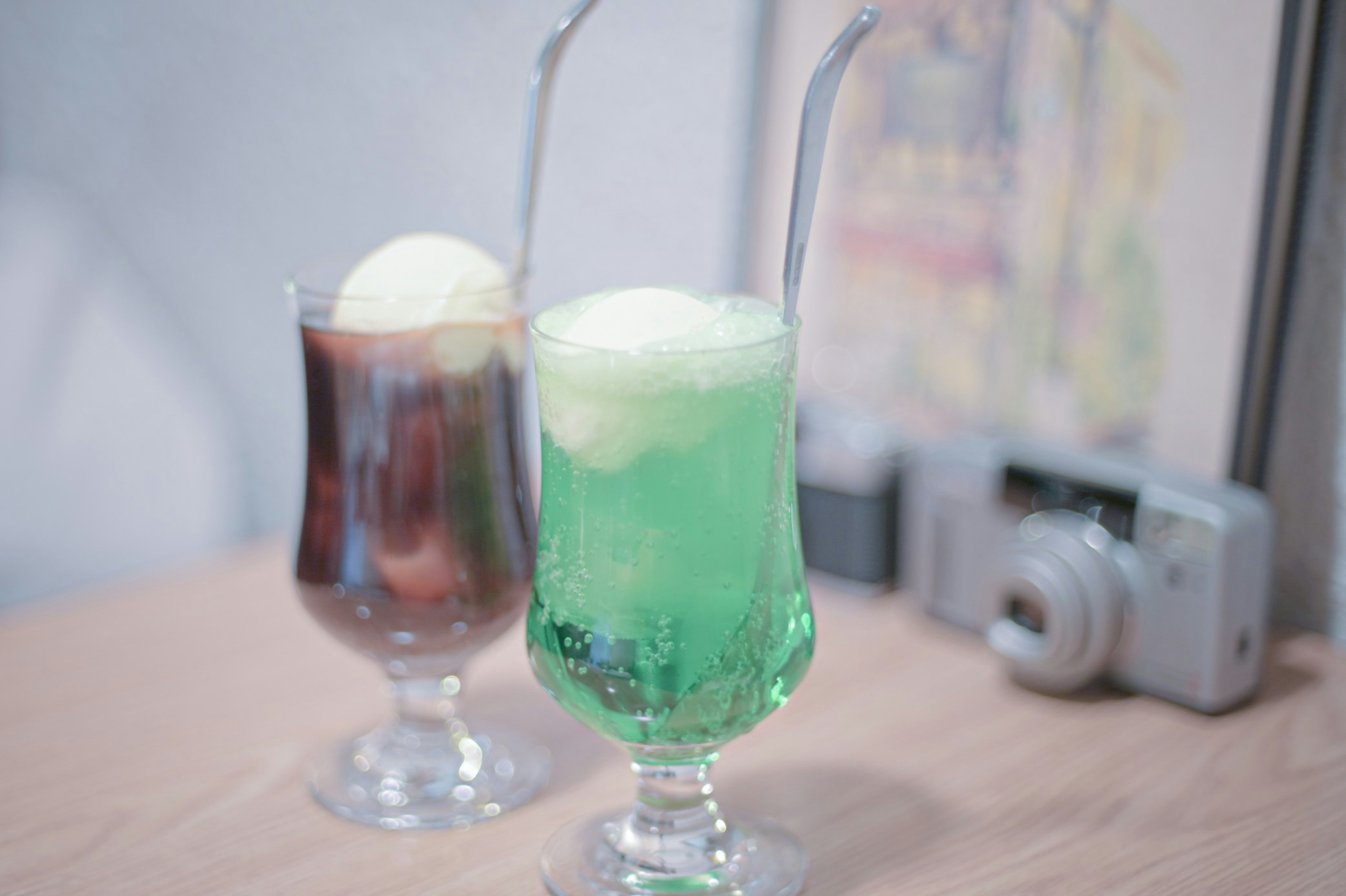 Two dessert drinks with green soda and ice cream on a wooden table