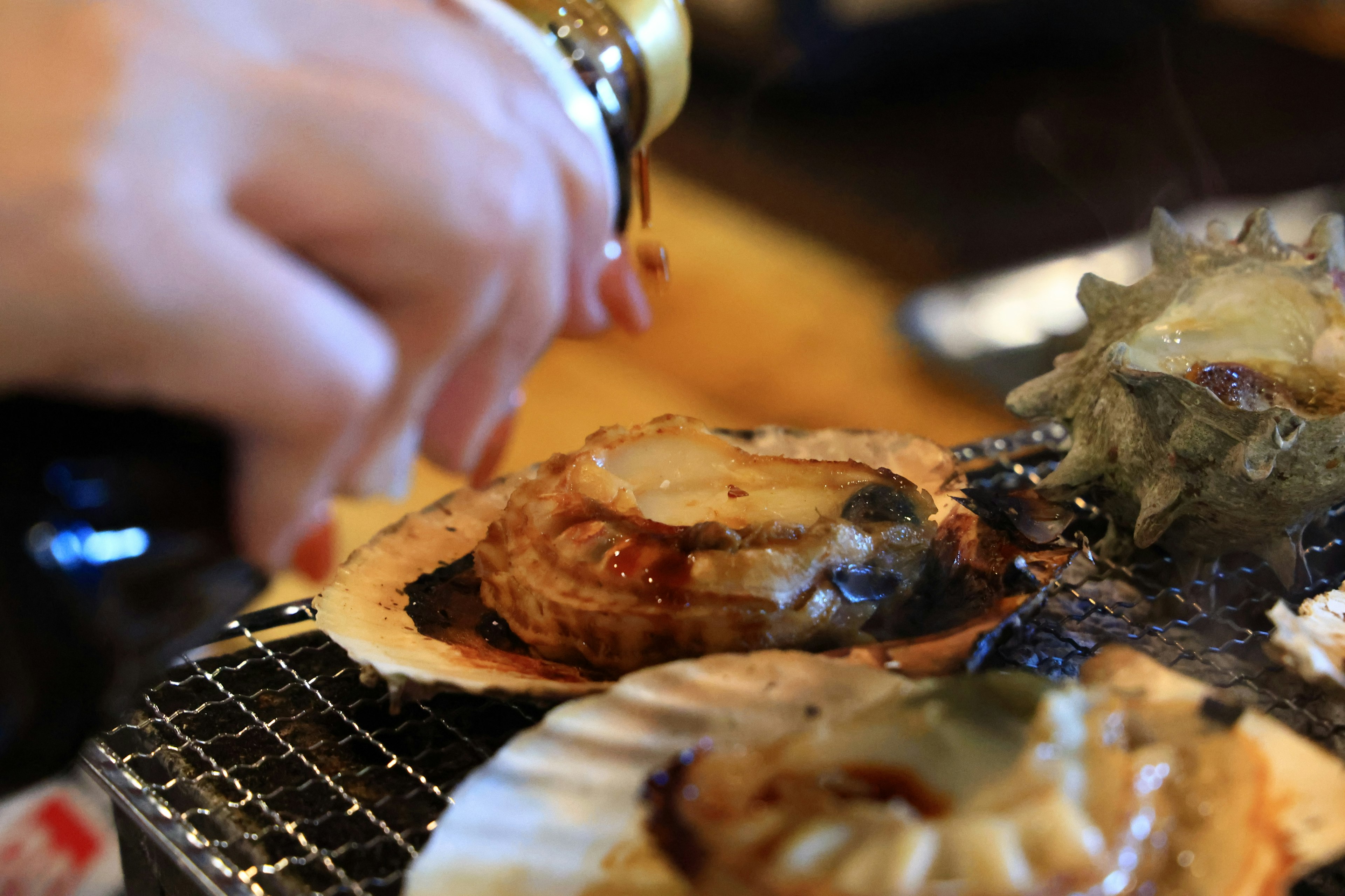 Tangan menuangkan saus di atas kerang bakar