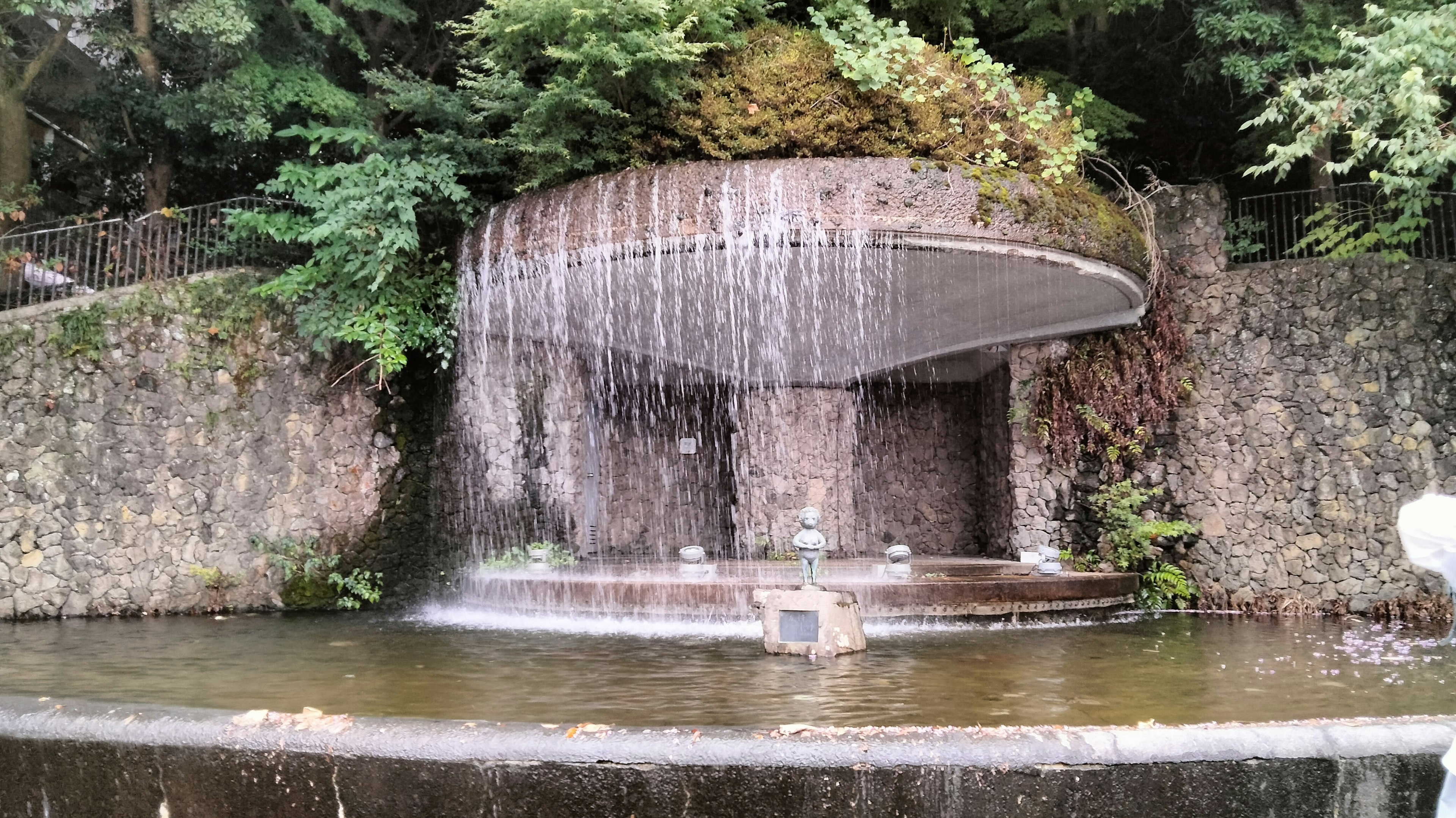 Una scena di parco serena con una cascata che scorre su una struttura di pietra circondata da una lussureggiante vegetazione