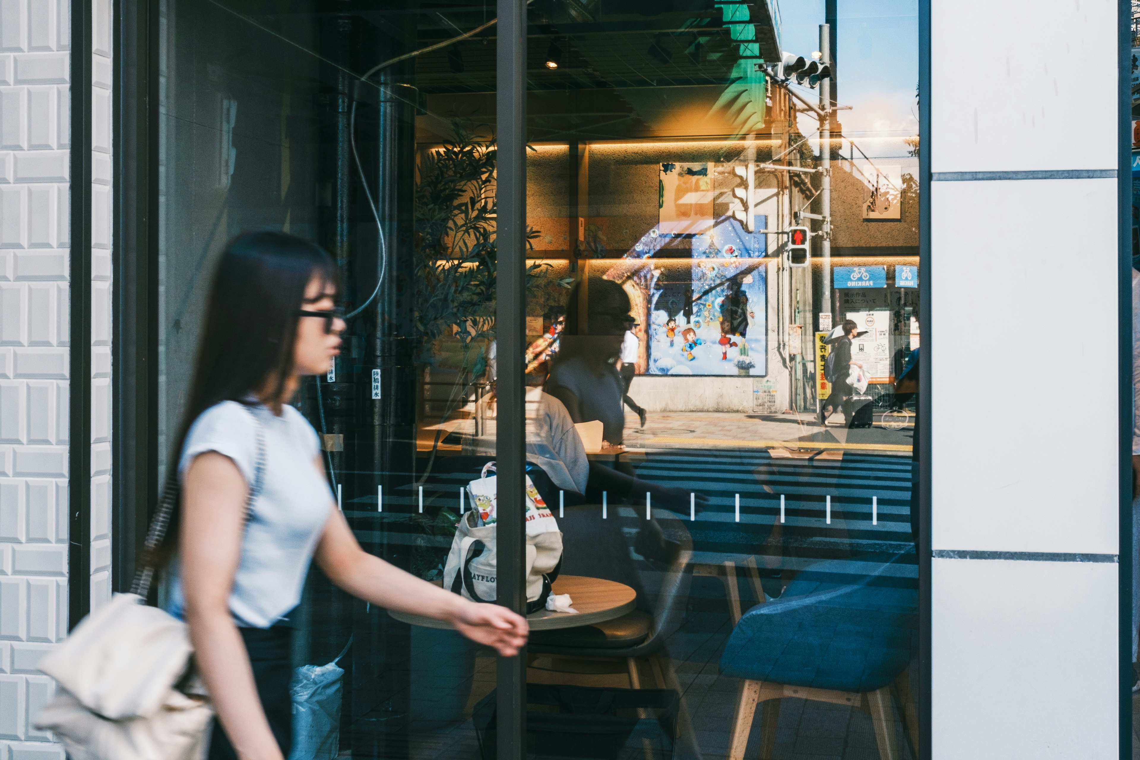 Eine Frau geht an einem Caféfenster vorbei mit Reflexionen des Innenraums und der Außenlandschaft