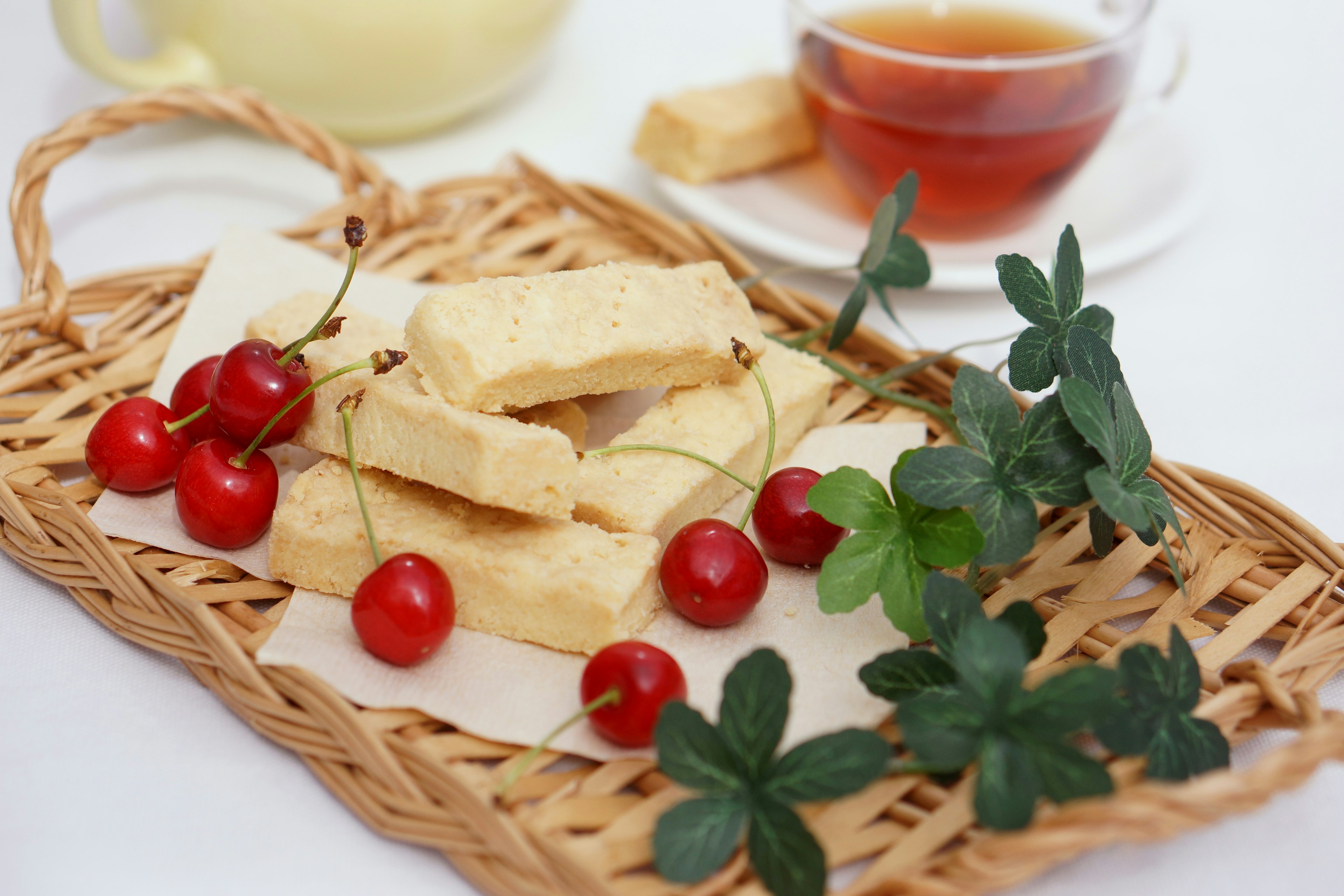 A basket with cookies cherries and mint leaves alongside tea