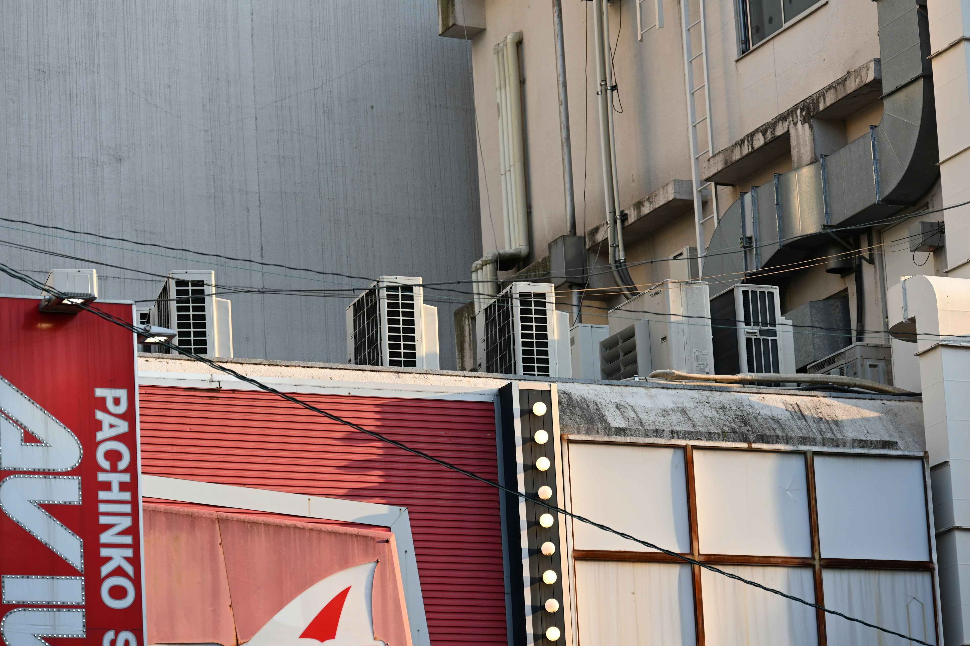 Coin d'un bâtiment avec un panneau de pachinko et plusieurs climatiseurs