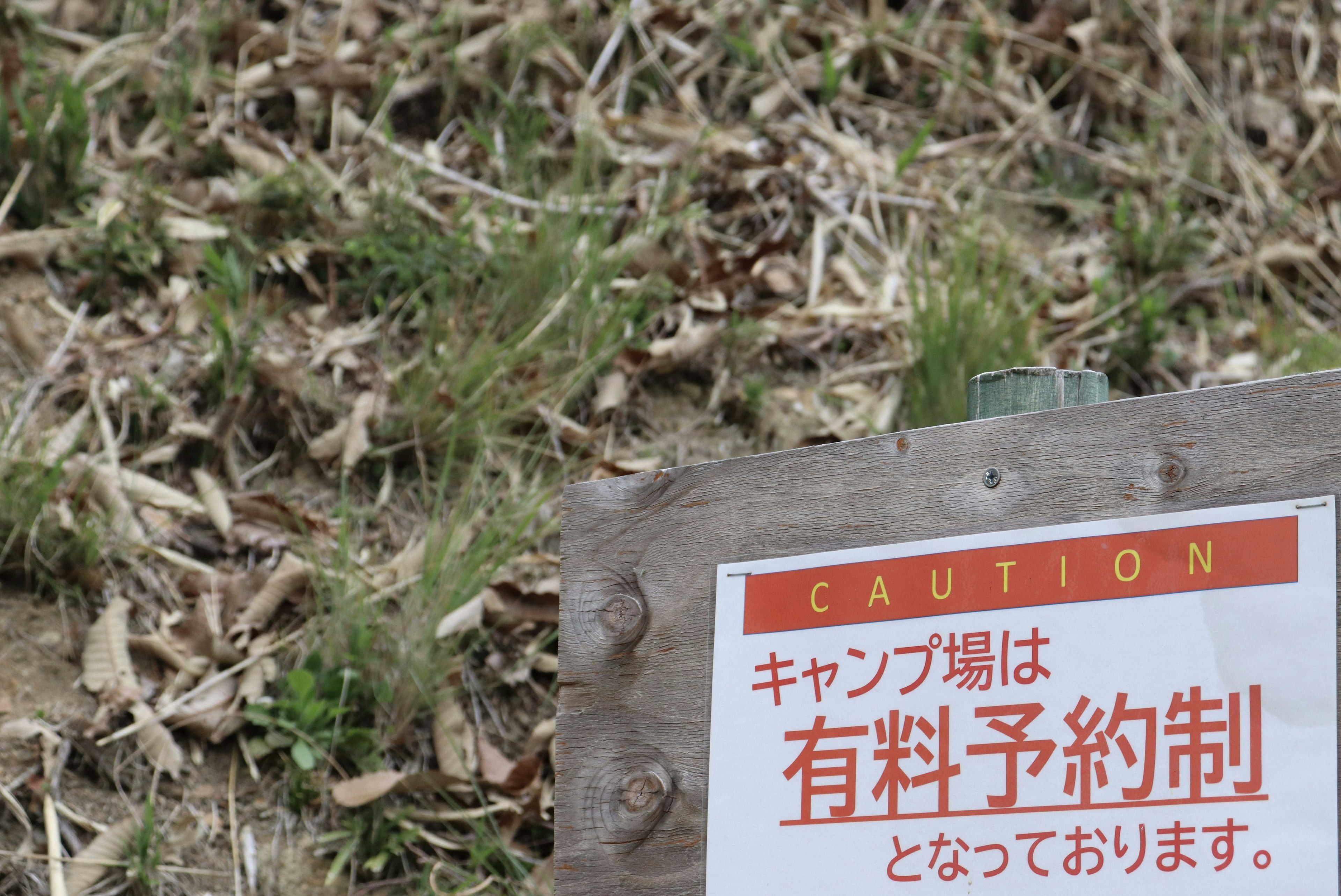 Caution sign indicating paid reservation required for camping area with grass background