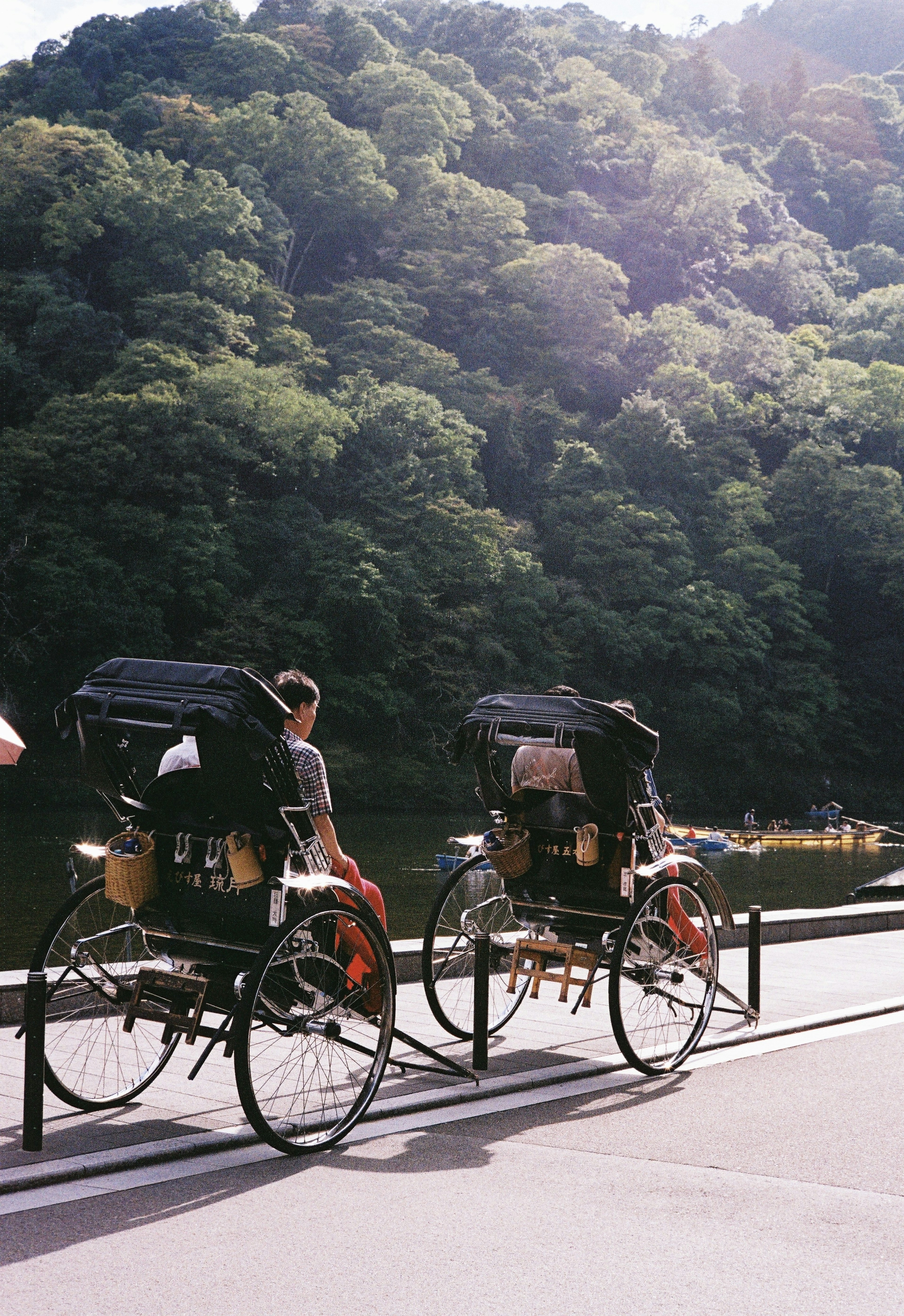 Rickshaws lined up by a river with a lush green mountain in the background