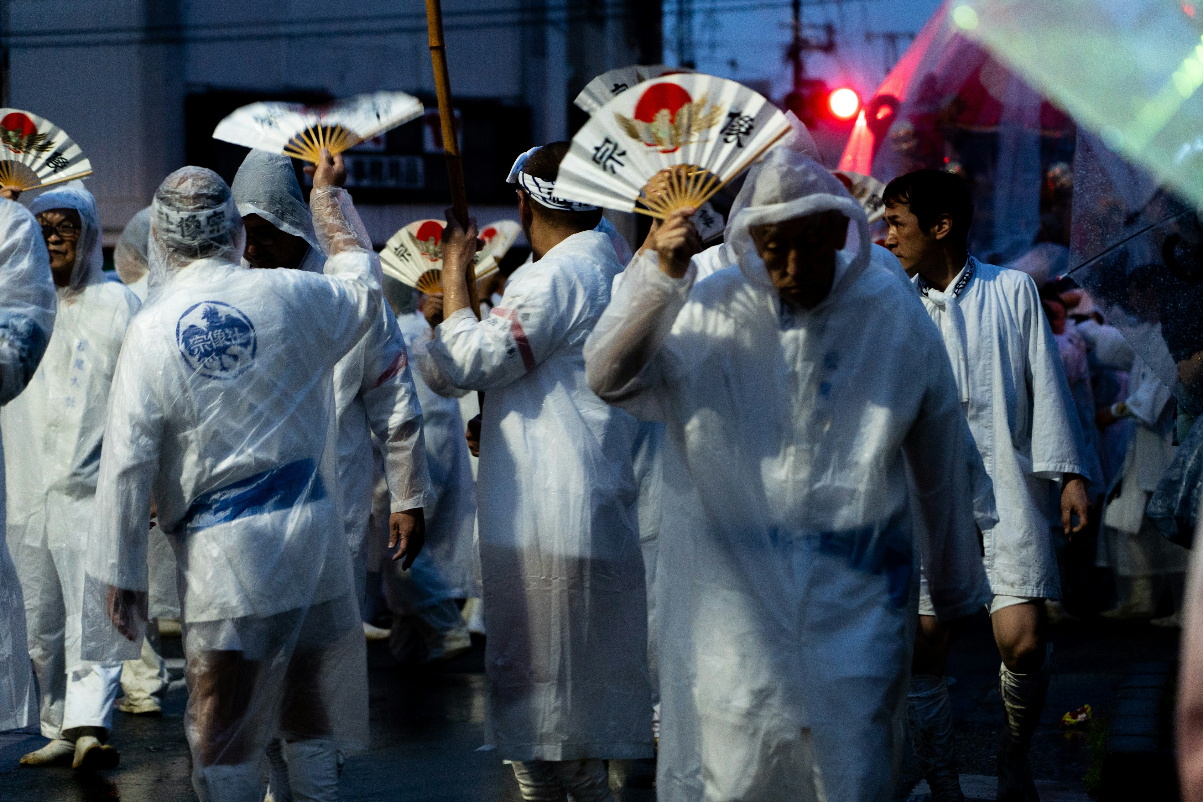 Processione di persone in impermeabili bianchi che tengono ventagli sotto la pioggia