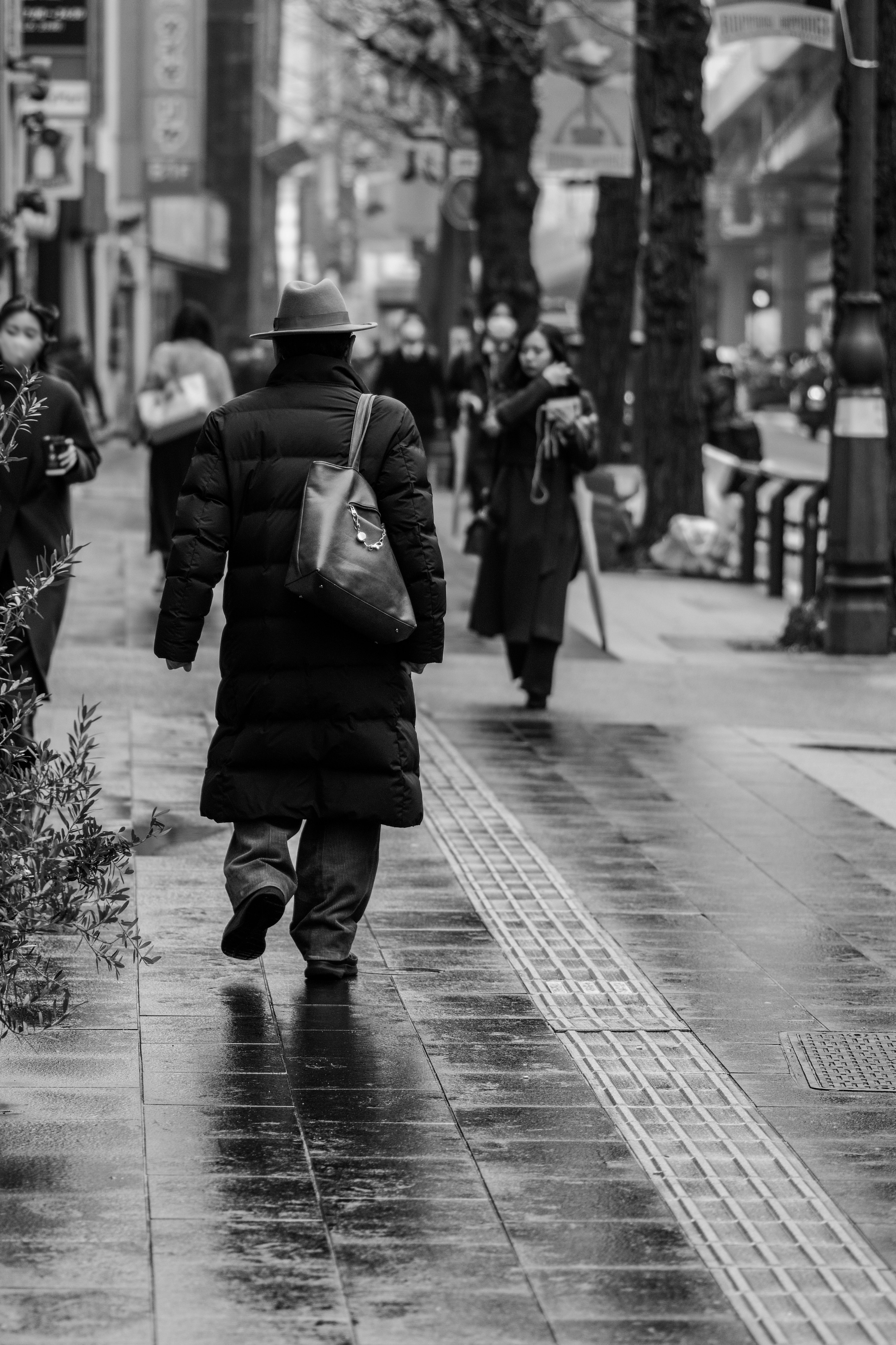 Scène de rue en noir et blanc avec des gens marchant et un trottoir mouillé