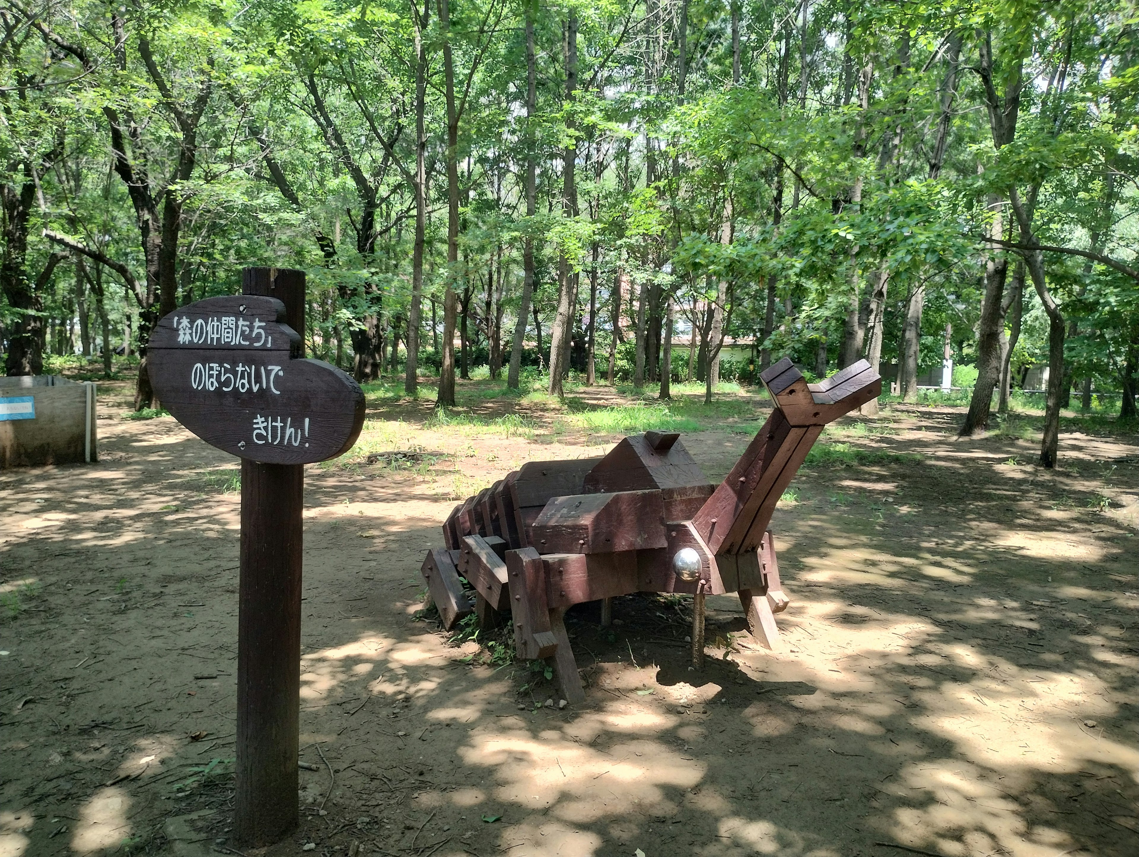 Patung dinosaurus kayu di taman yang dikelilingi pohon