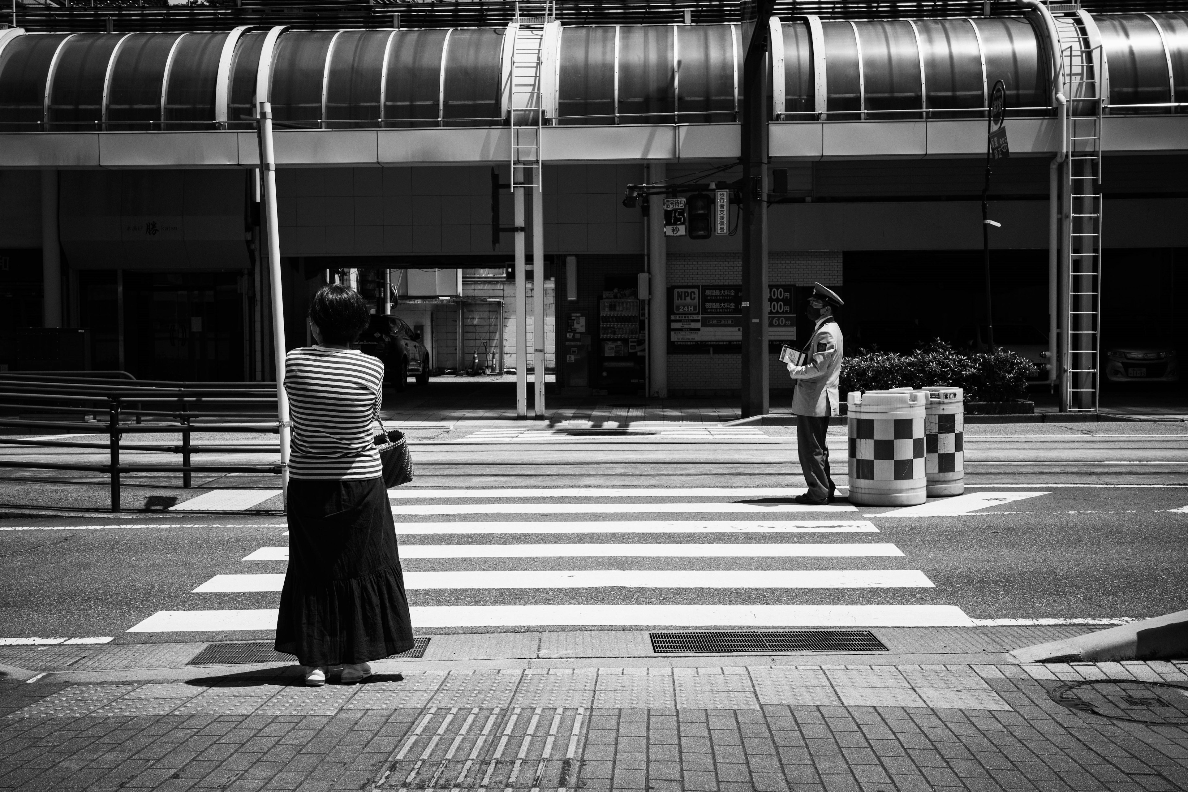 Una mujer esperando en un paso de cebra junto a un hombre en blanco y negro