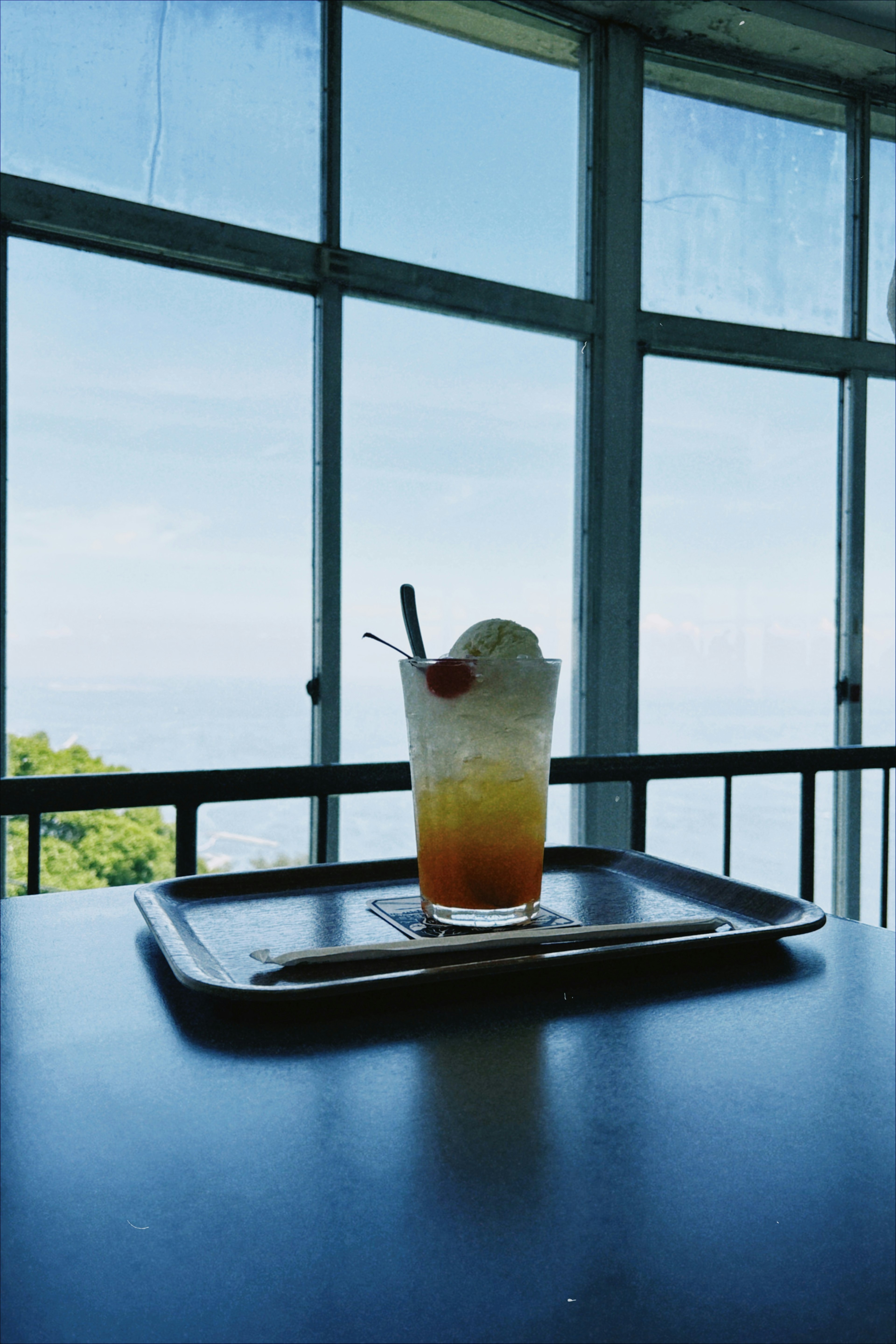 Colorful drink on a tray at a cafe table with a view of the sky and greenery