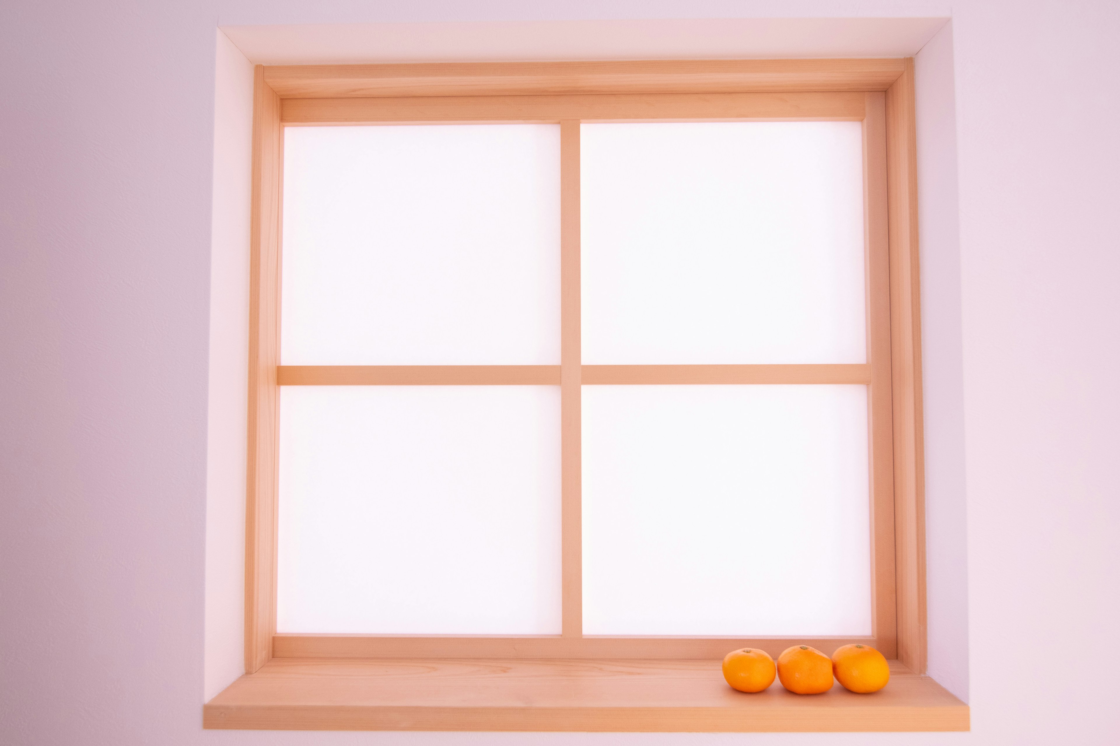 Ein Holzfensterrahmen mit weißen Glasscheiben und Orangen auf der Fensterbank