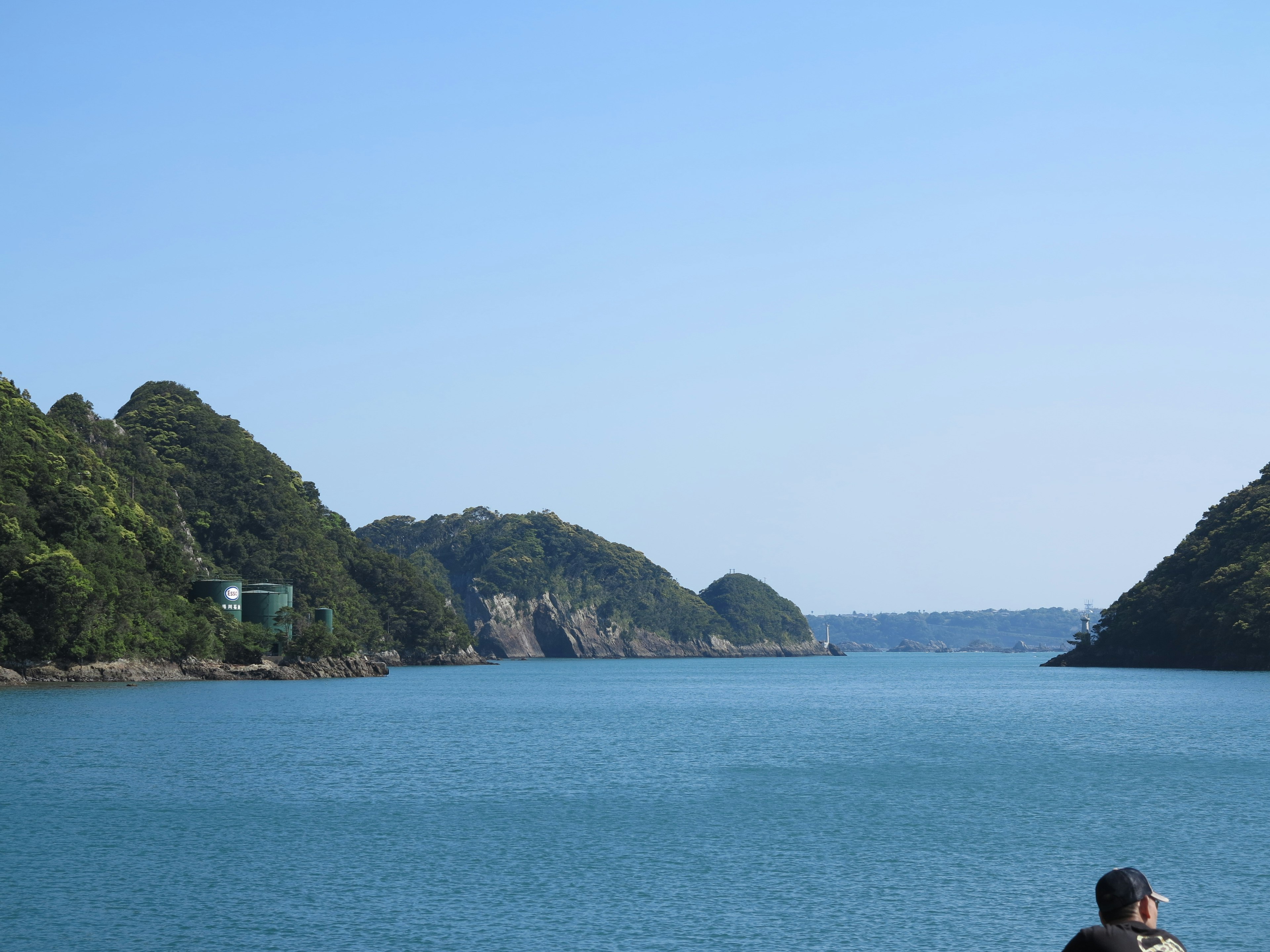 青い海と緑の山々が広がる風景で、静かな湾に人が座っている