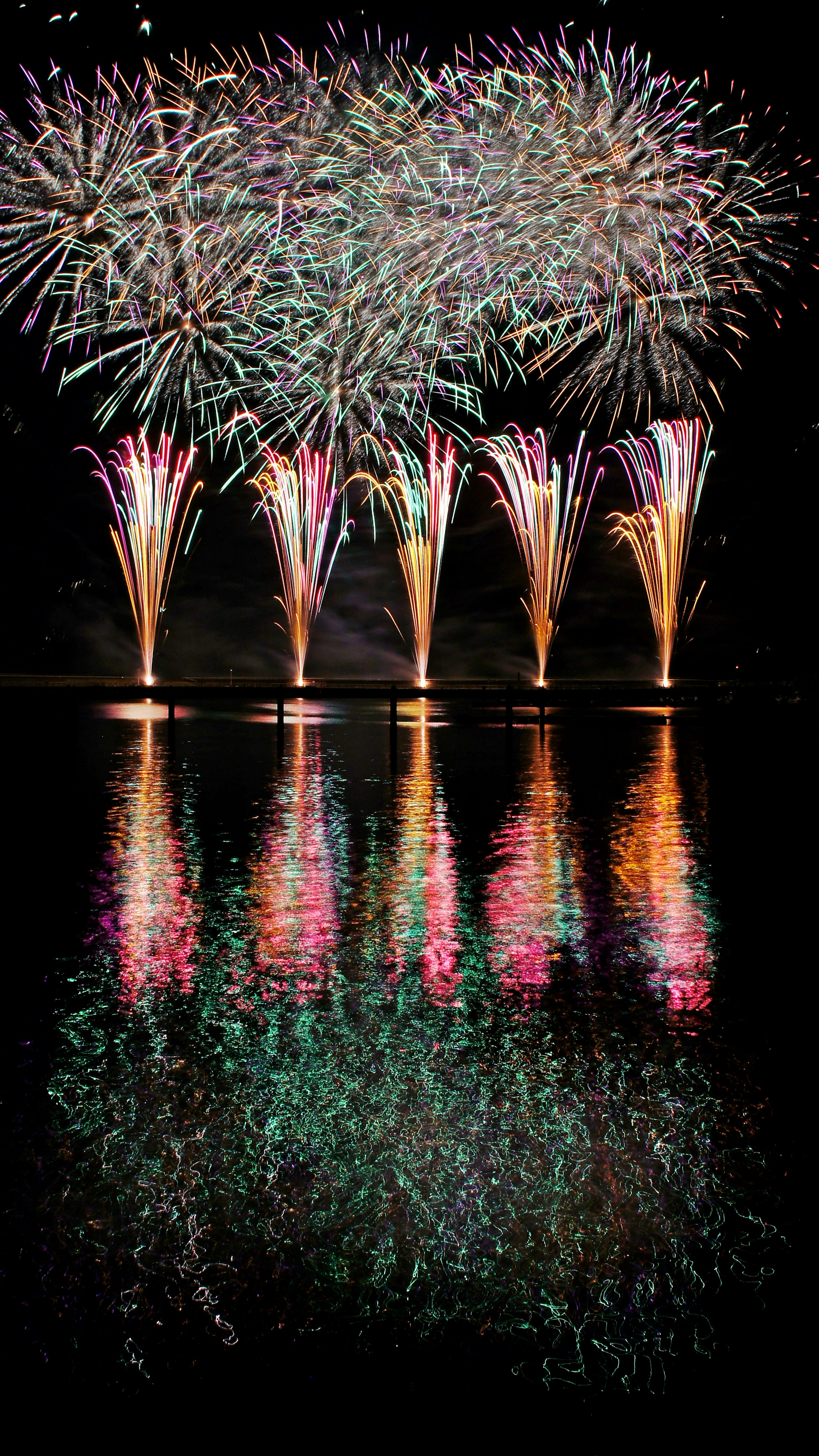 Colorful fireworks display in the night sky reflecting on water