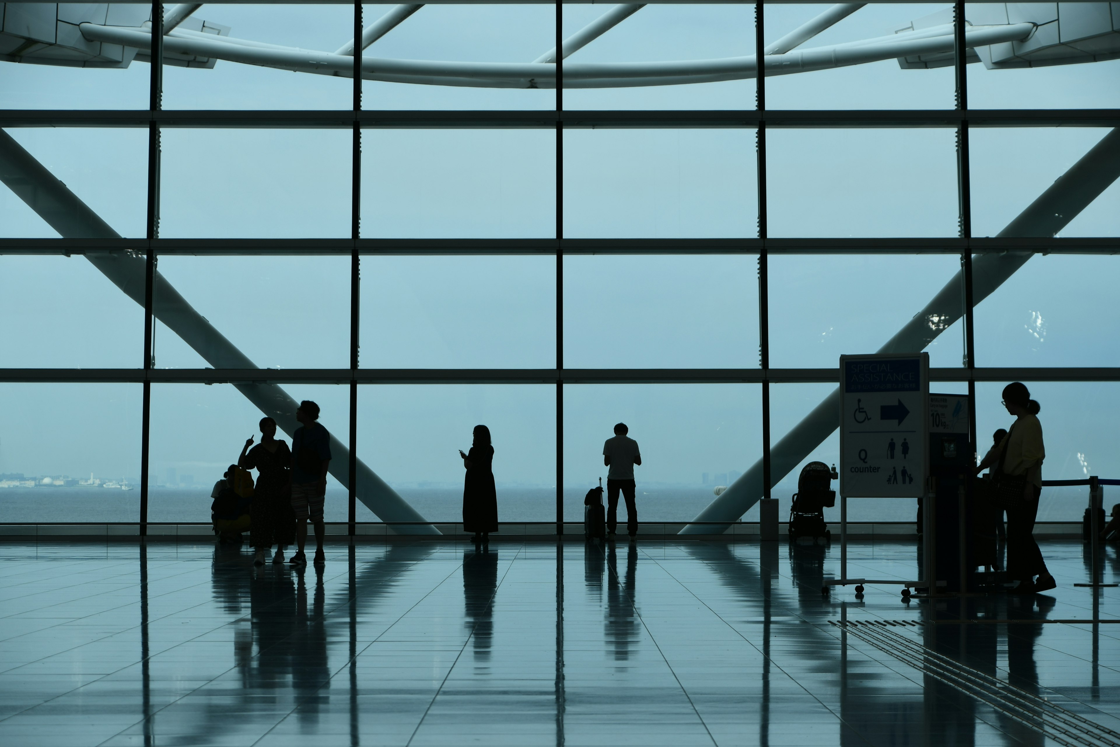 Siluetas de personas frente a grandes ventanas del aeropuerto con reflejos