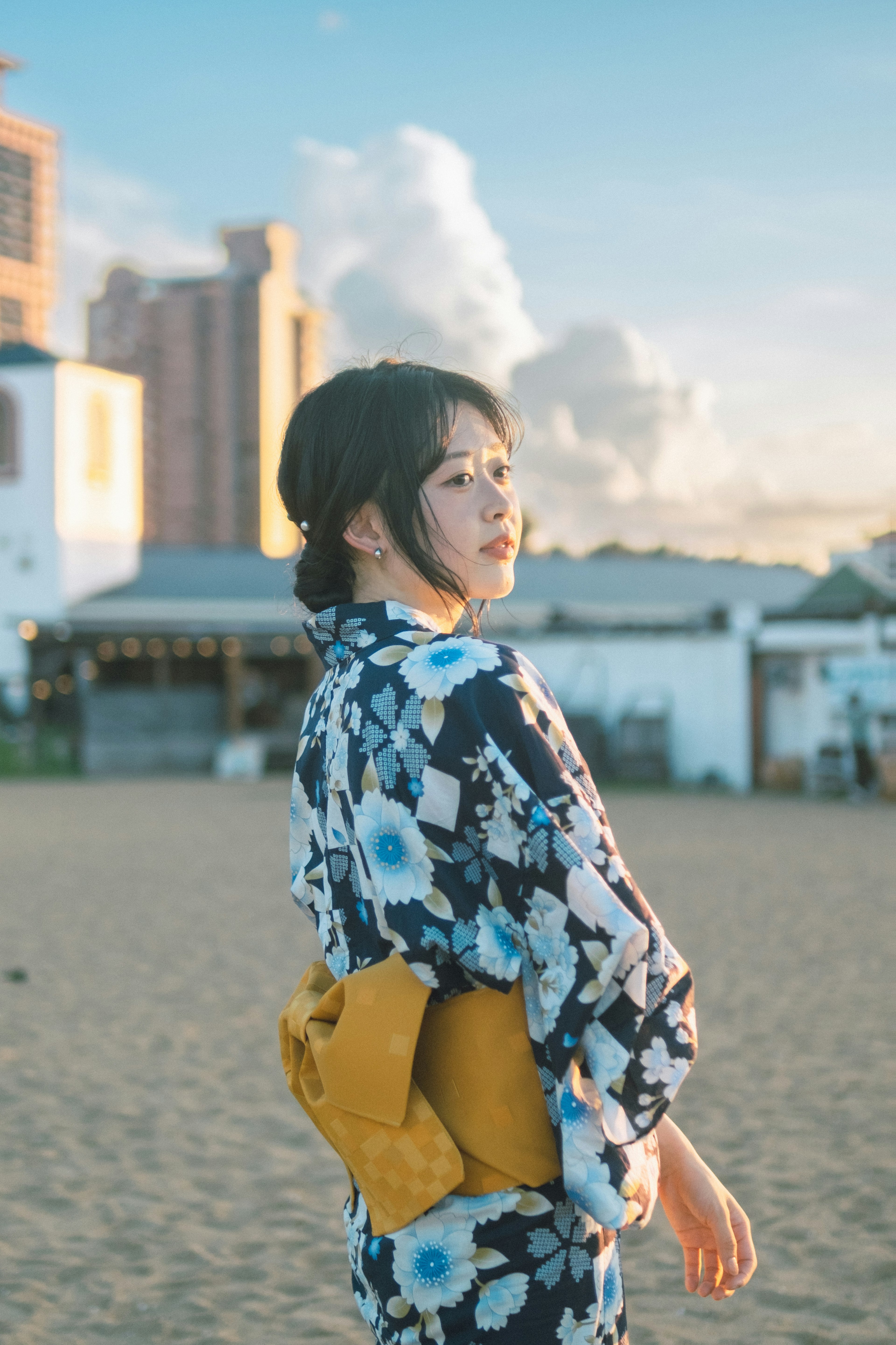 Seorang wanita dalam yukata berbunga berdiri di pantai dengan latar belakang matahari terbenam