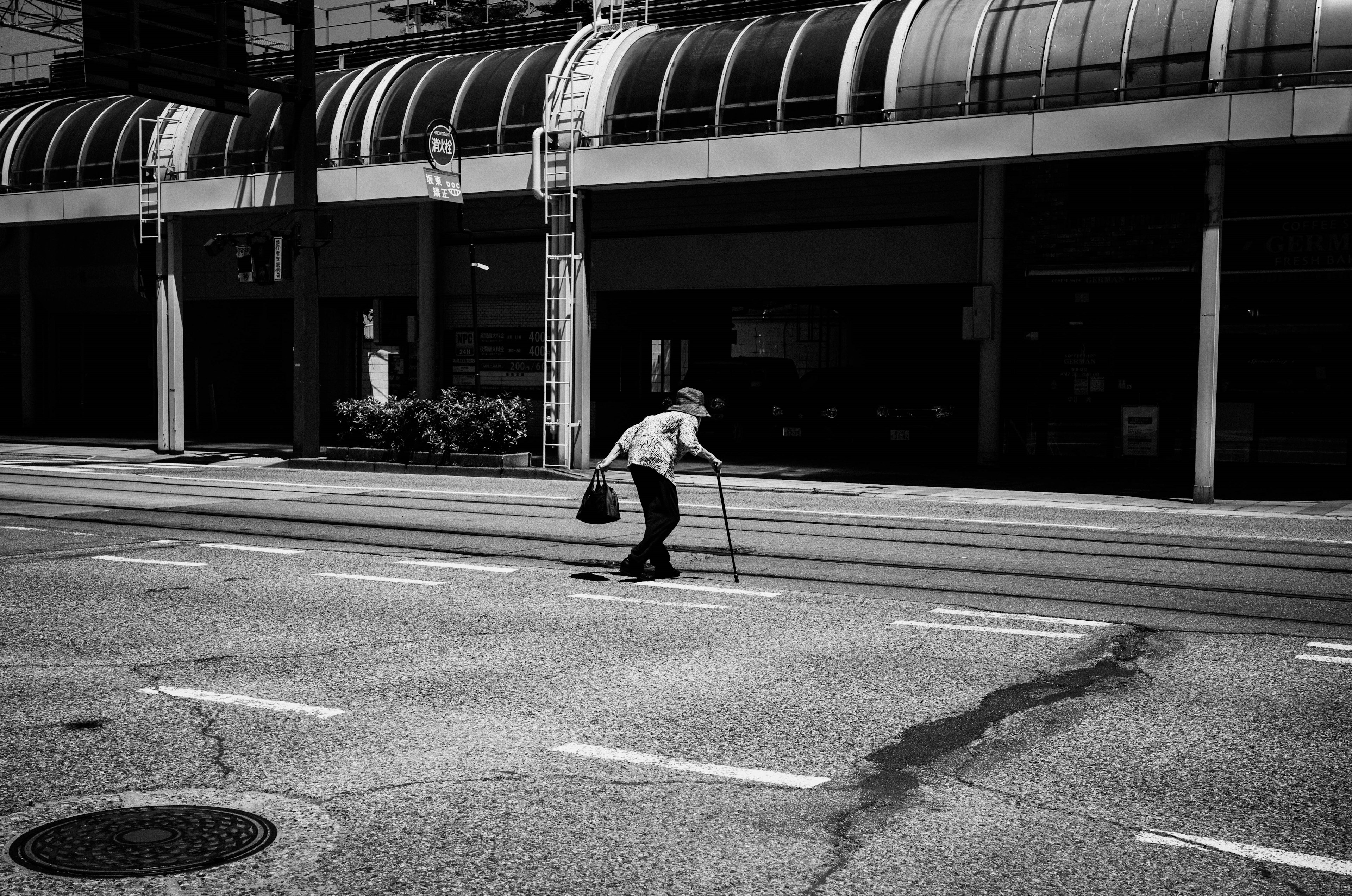 Elderly person walking with a cane in a black and white urban setting