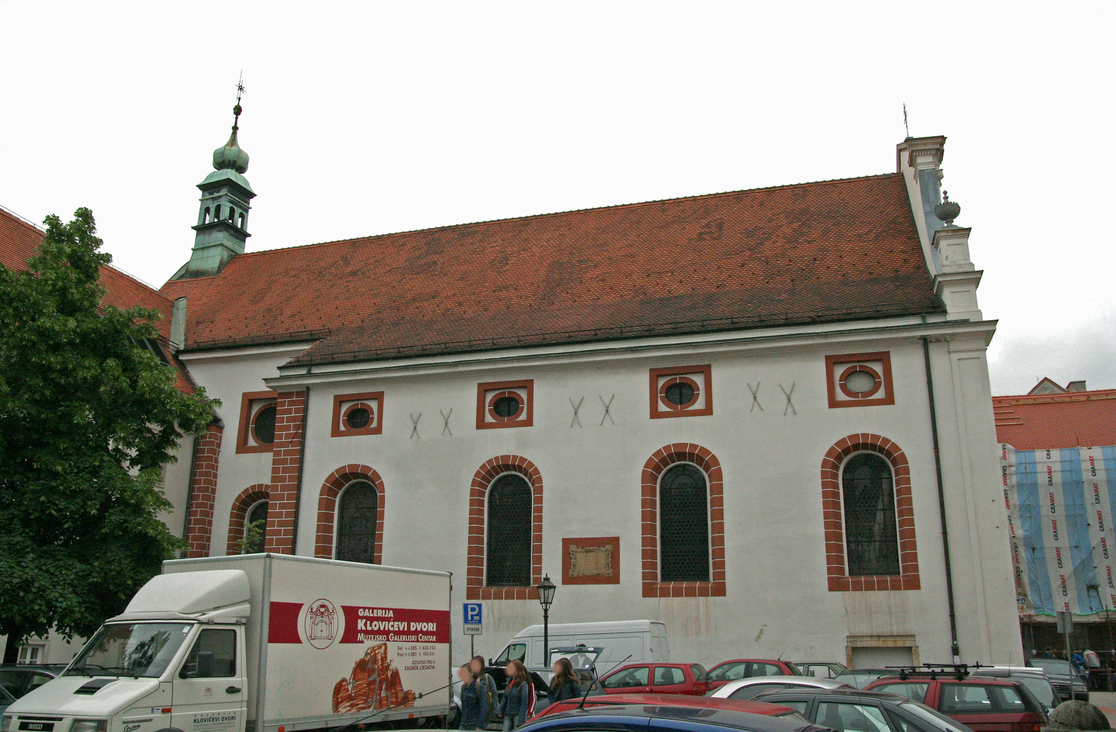 Außenansicht einer Kirche mit weißen Wänden und rotem Dach geparkter Lastwagen und Autos in der Nähe