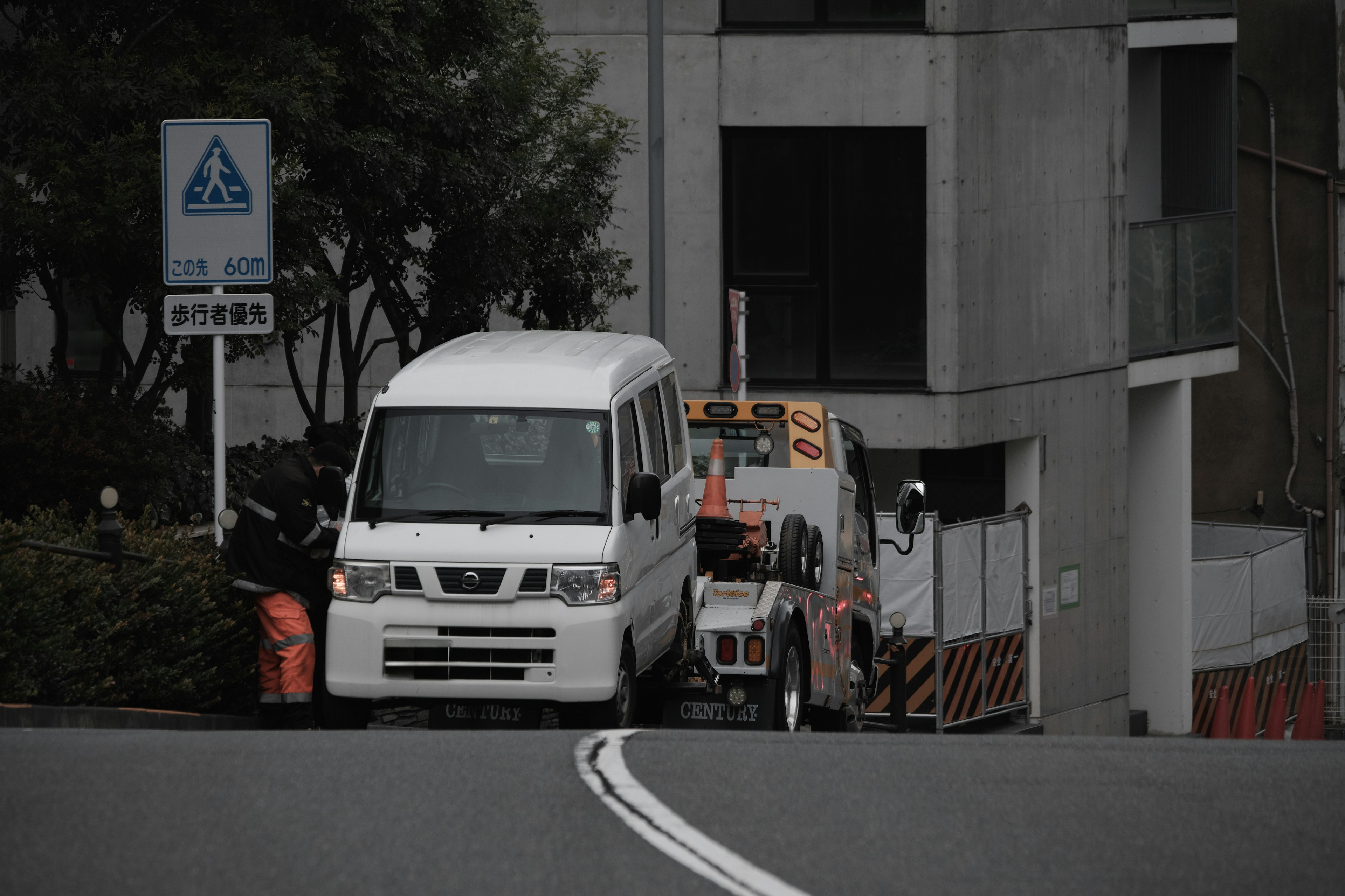 一輛白色廂型車停在狹窄的道路上，後面是一輛卡車，周圍是城市風景