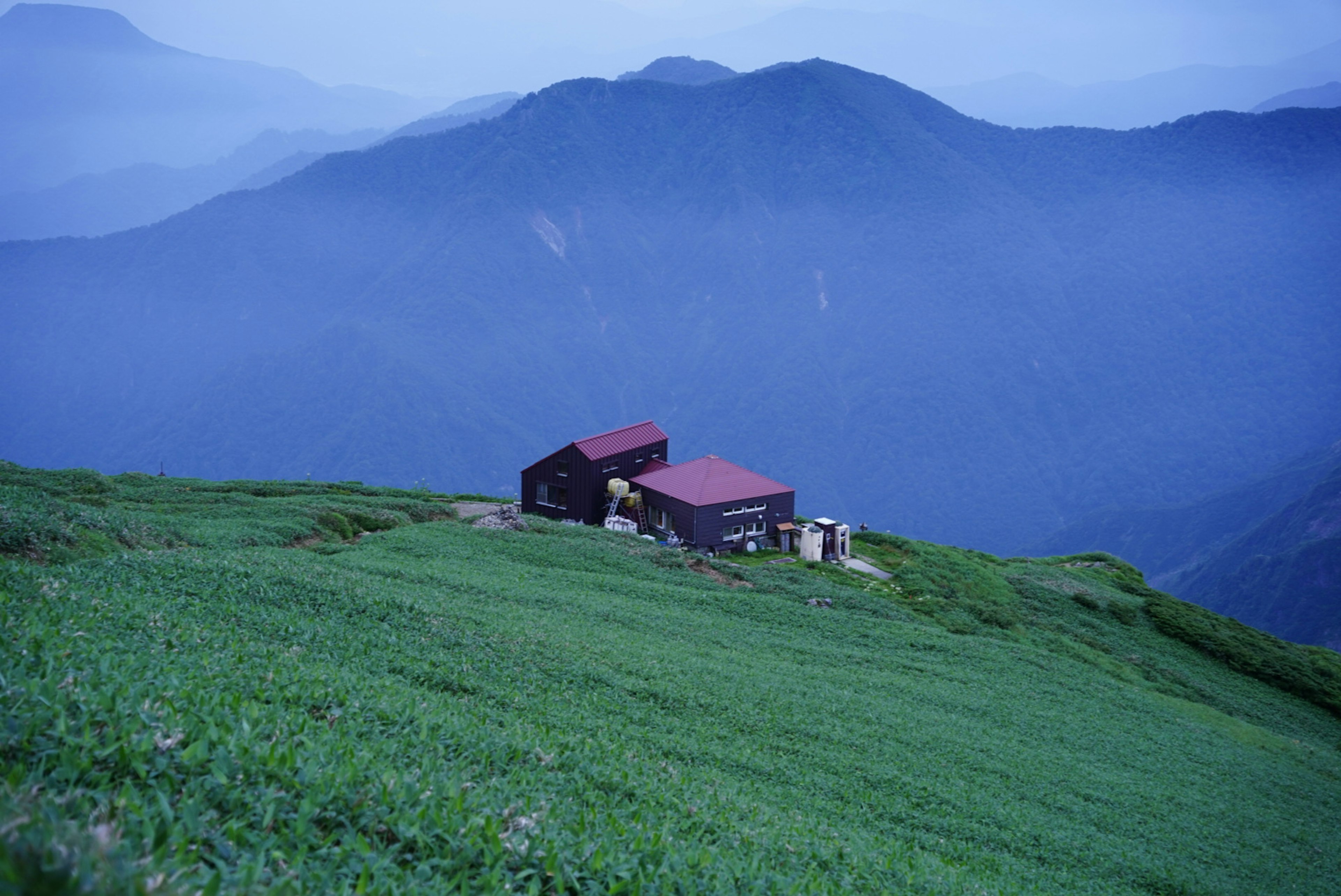 Un petit chalet de montagne entouré de montagnes bleues et de verdure