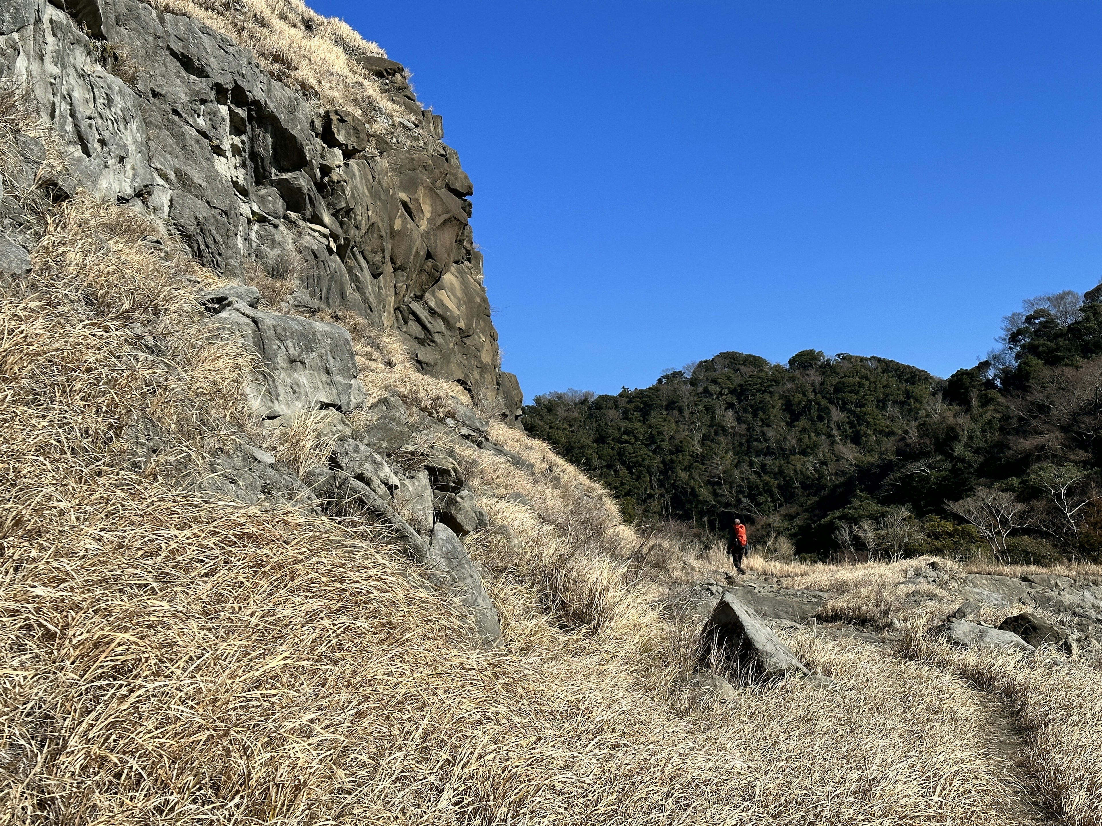 A person walking beside a large rock in a dry grassland under a blue sky