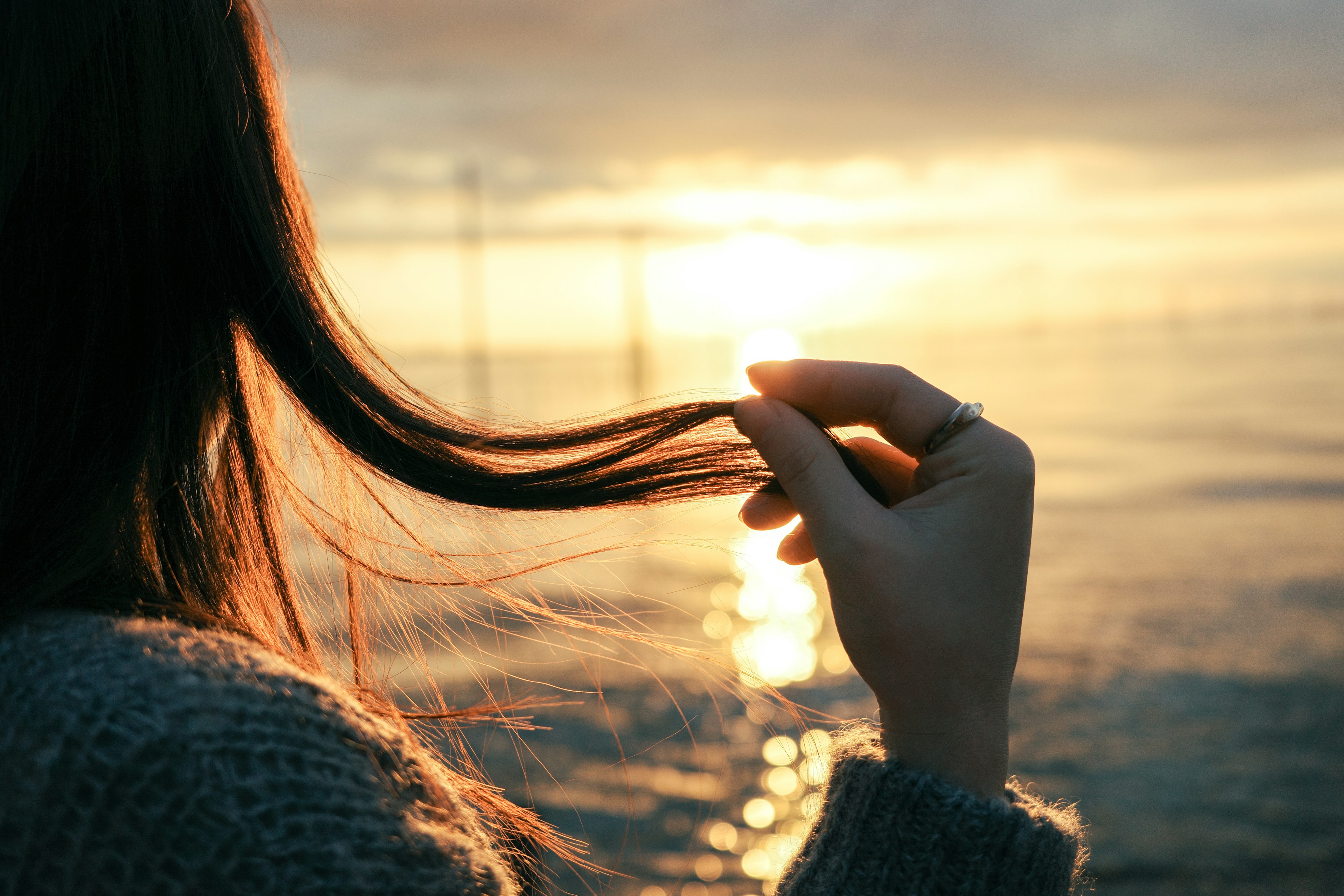 Une femme touchant ses cheveux avec un coucher de soleil en arrière-plan