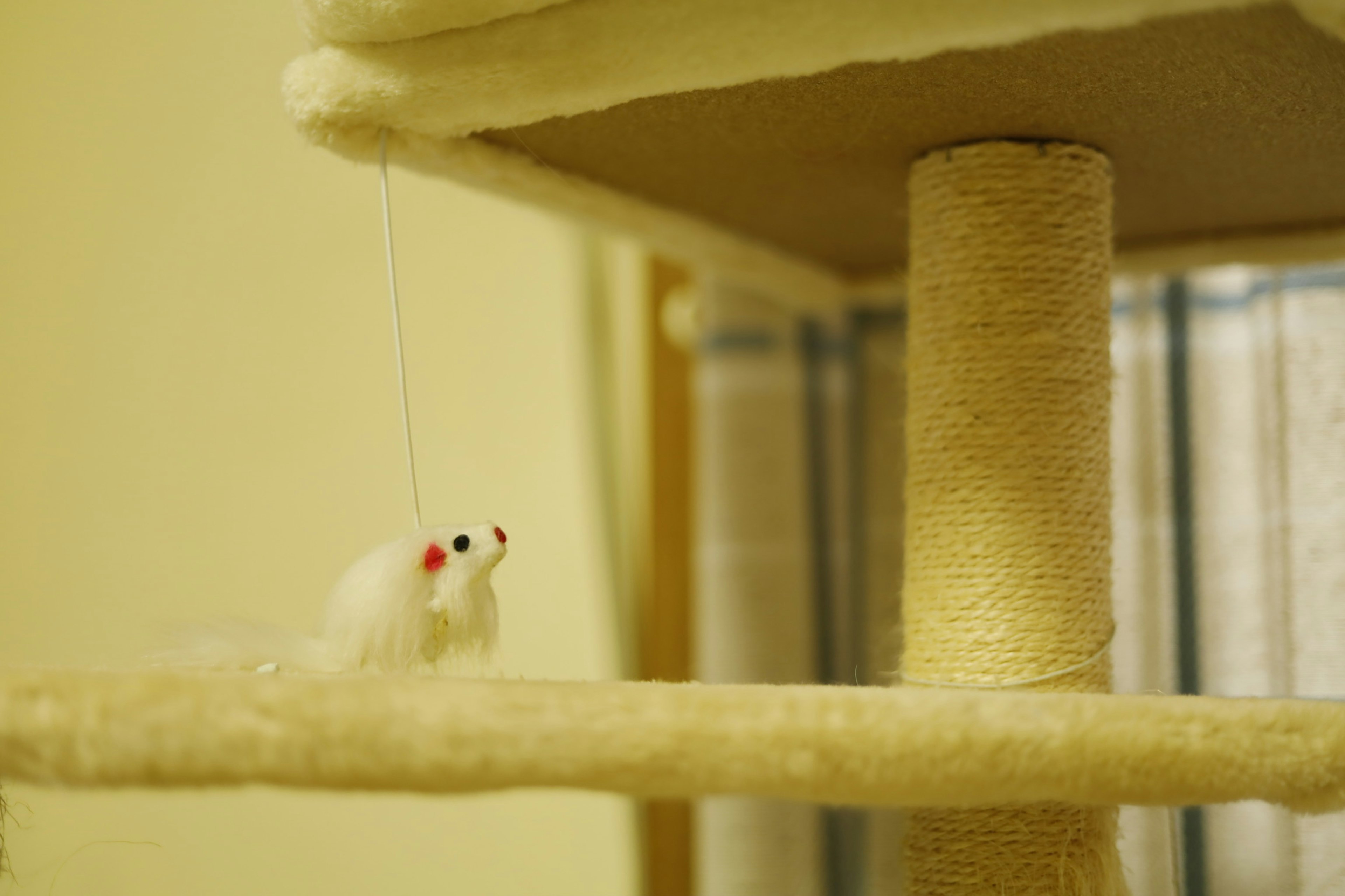 A section of a cat tree with a white mouse toy hanging from a string