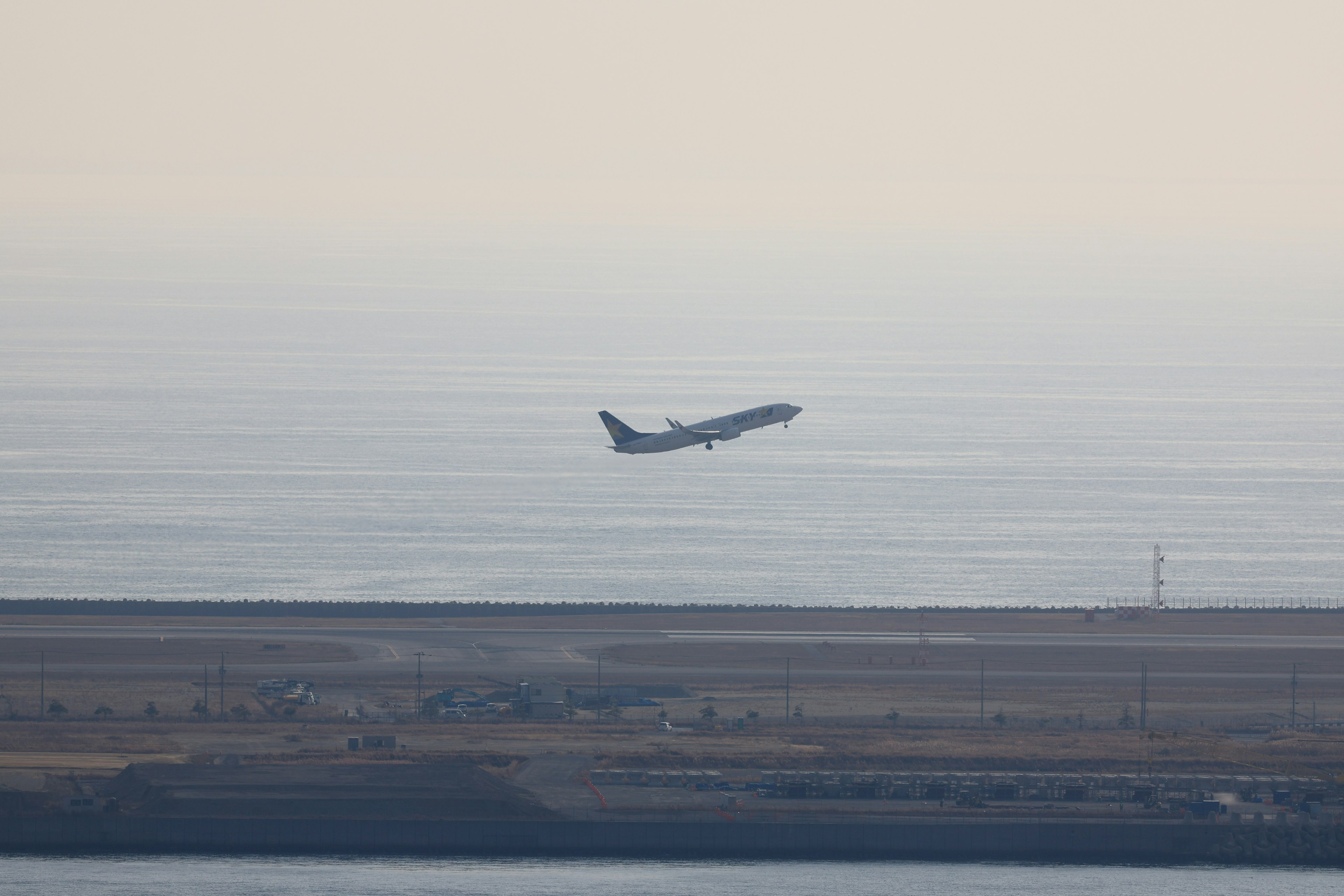 A distant view of an airplane taking off over the ocean